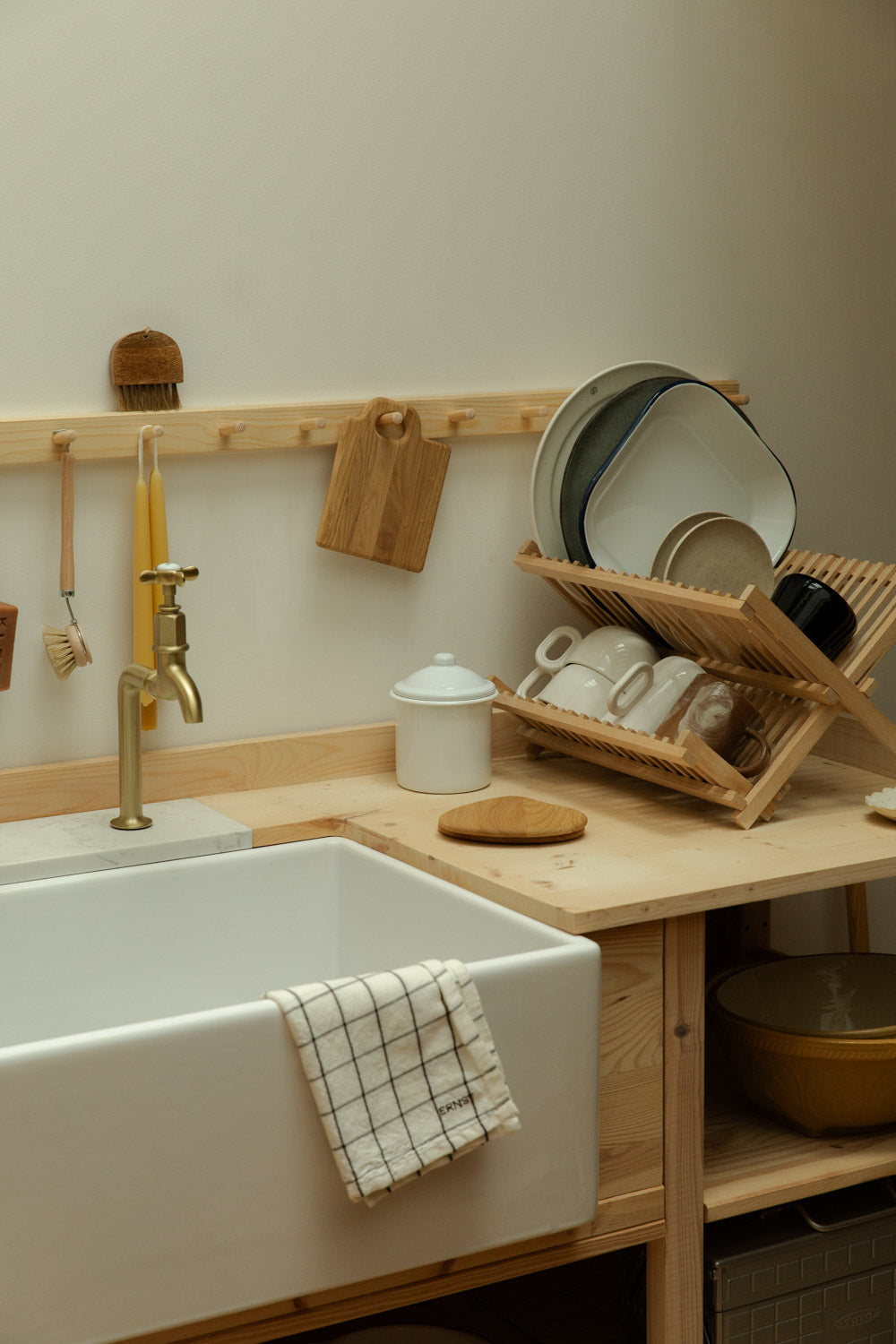 wooden kitchen with white belfast sink, wooden draining rack and cups, plates and boards.