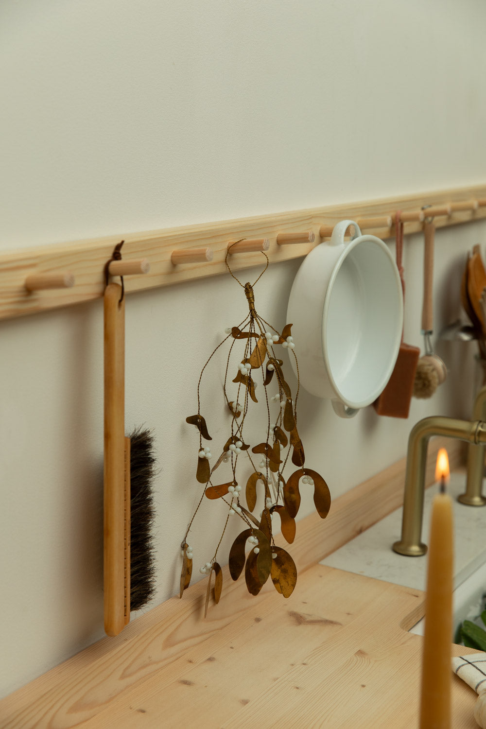 Kitchen wall with wooden rack holding a white mug, brush, and decorative branch.