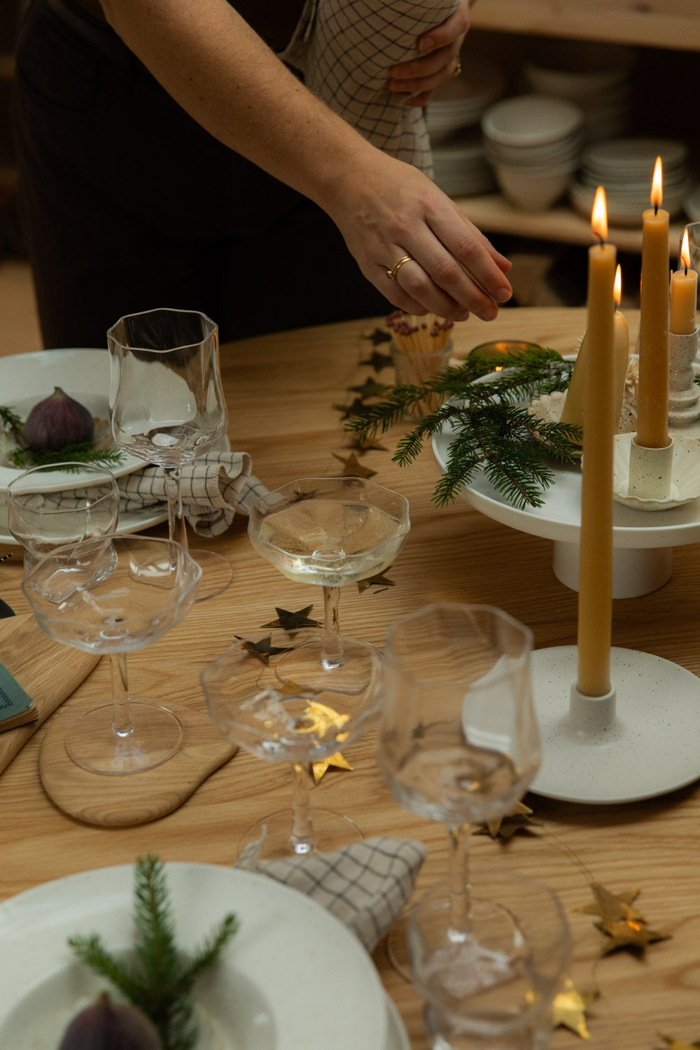 Decorative table setting with wine glasses, candles, and greenery on a wooden table.