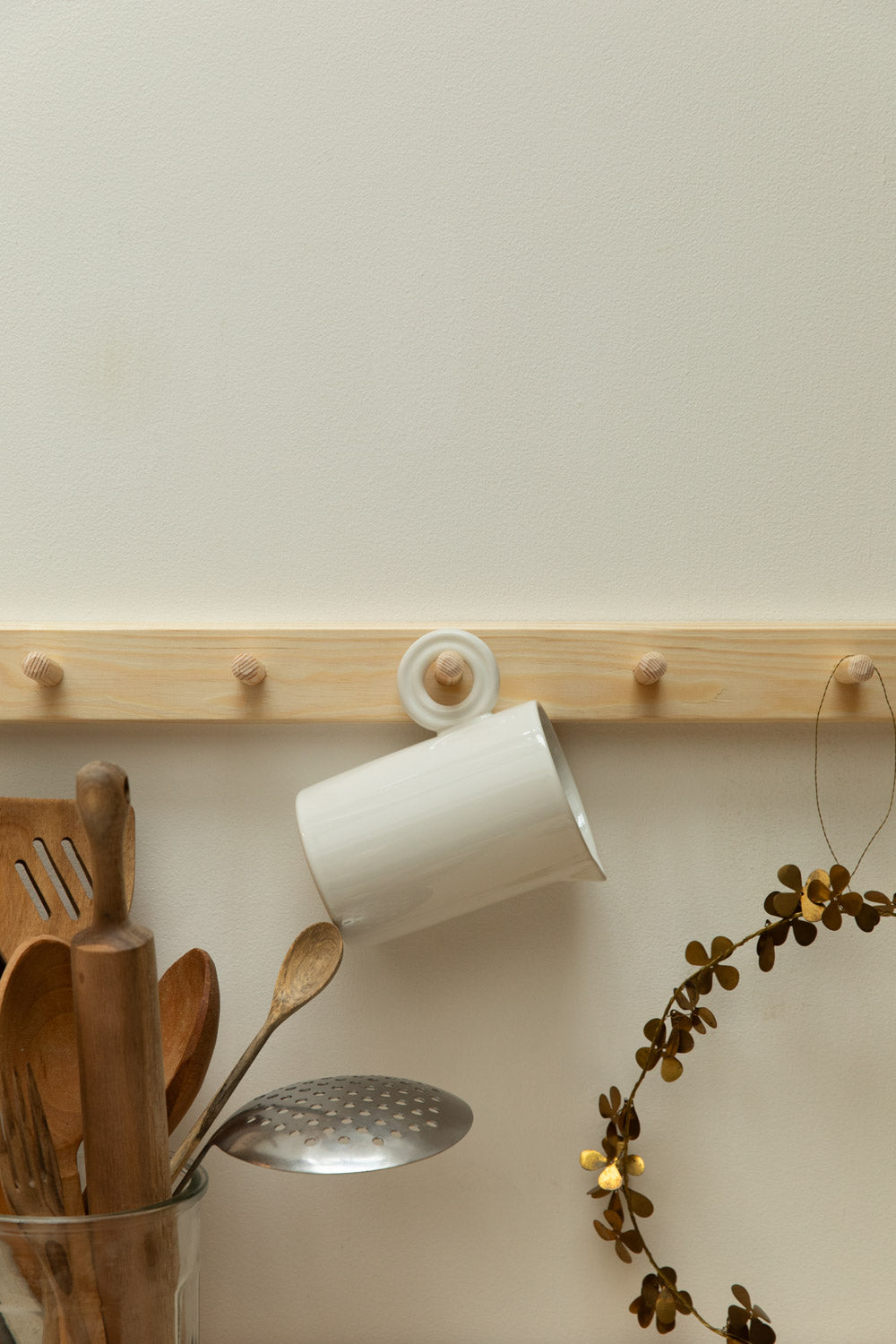Wooden pegrail with kitchen utensils and a white jug on a light wall.
