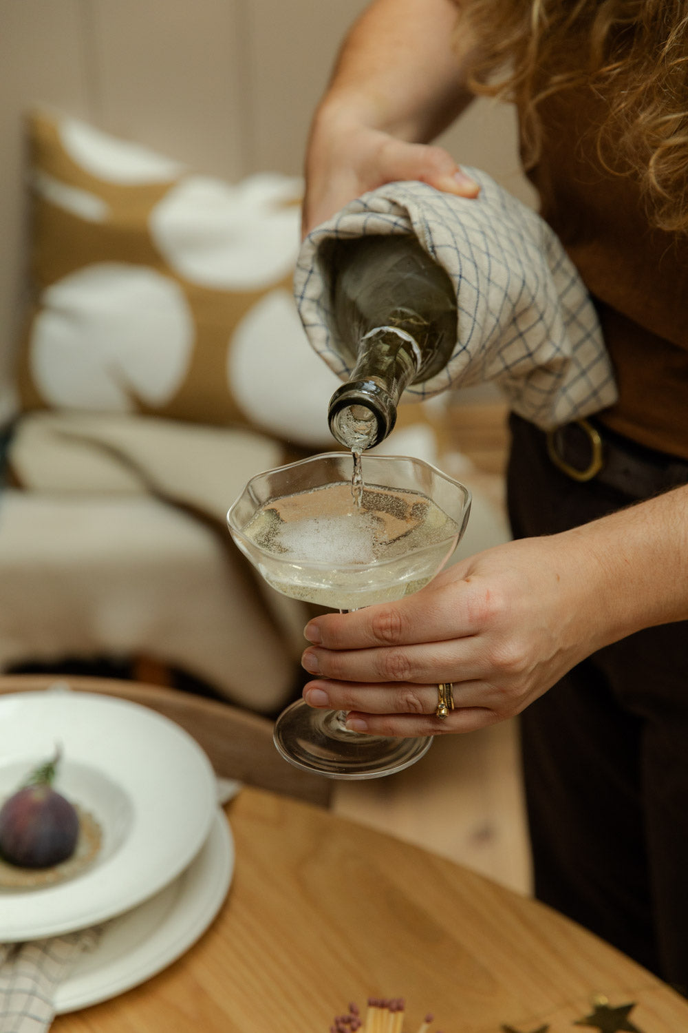 Person pouring a drink into a glass on a wooden table with a blurred background