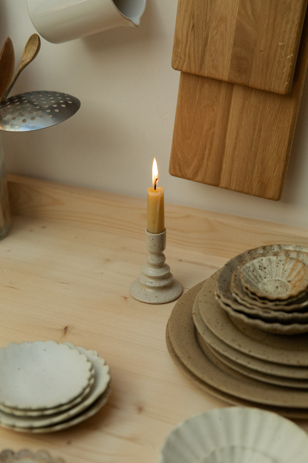 Candle in a rustic holder on a wooden surface with ceramic plates and bowls.
