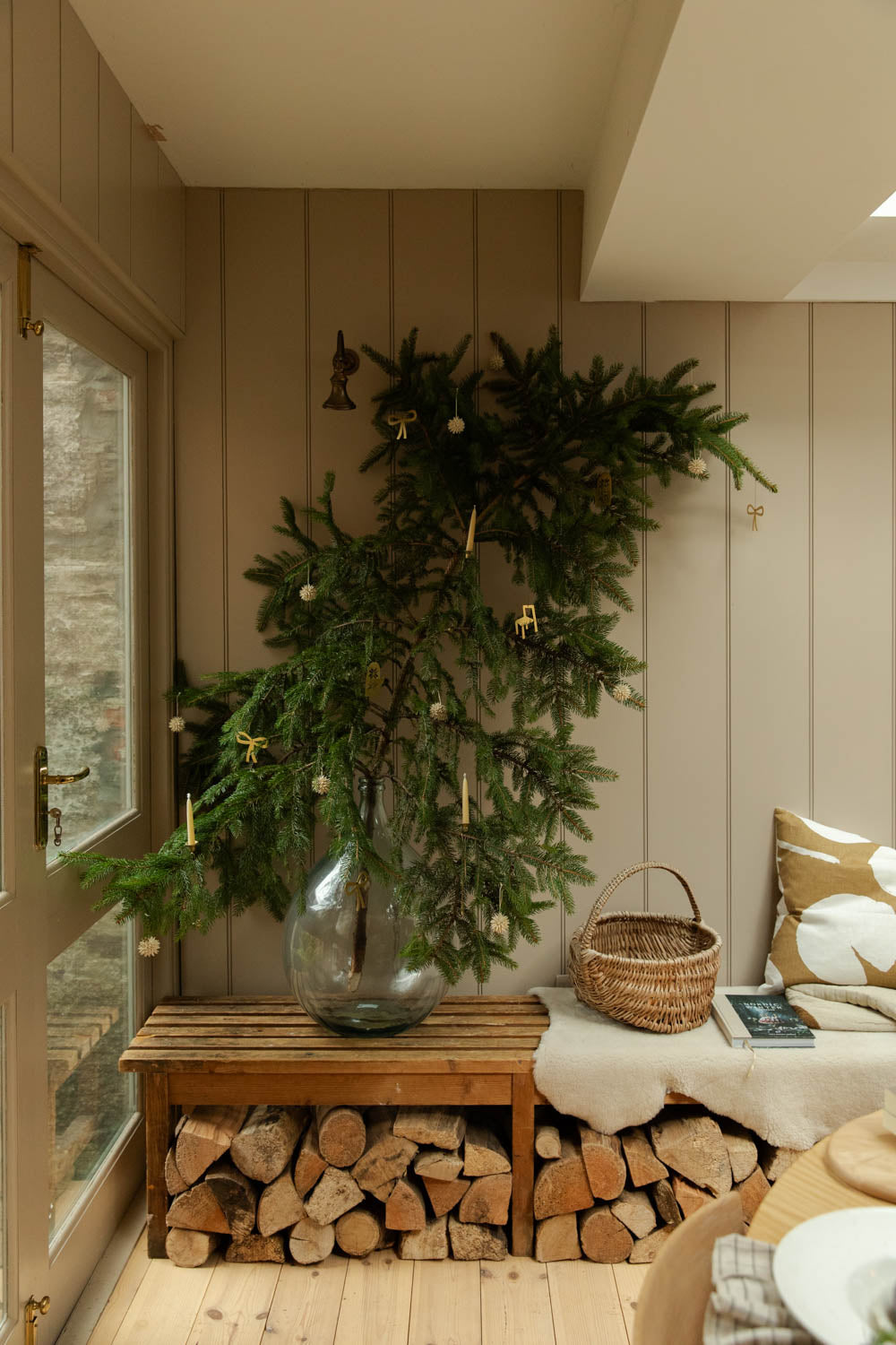 Decorative indoor setting with a fir branch, logs, and a bench.
