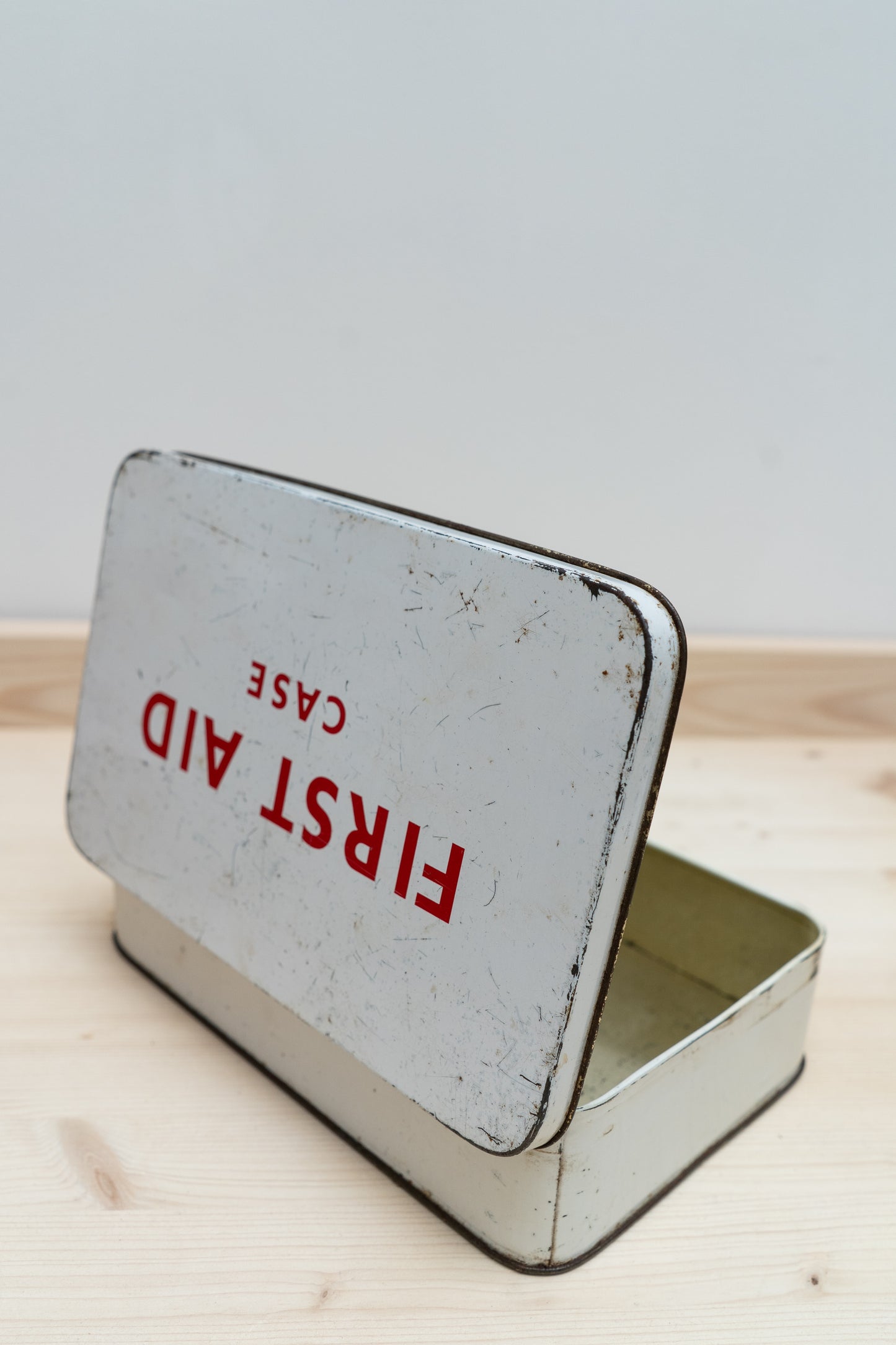 Vintage-style first aid tin with 'First Aid Case' text on a light wooden surface.