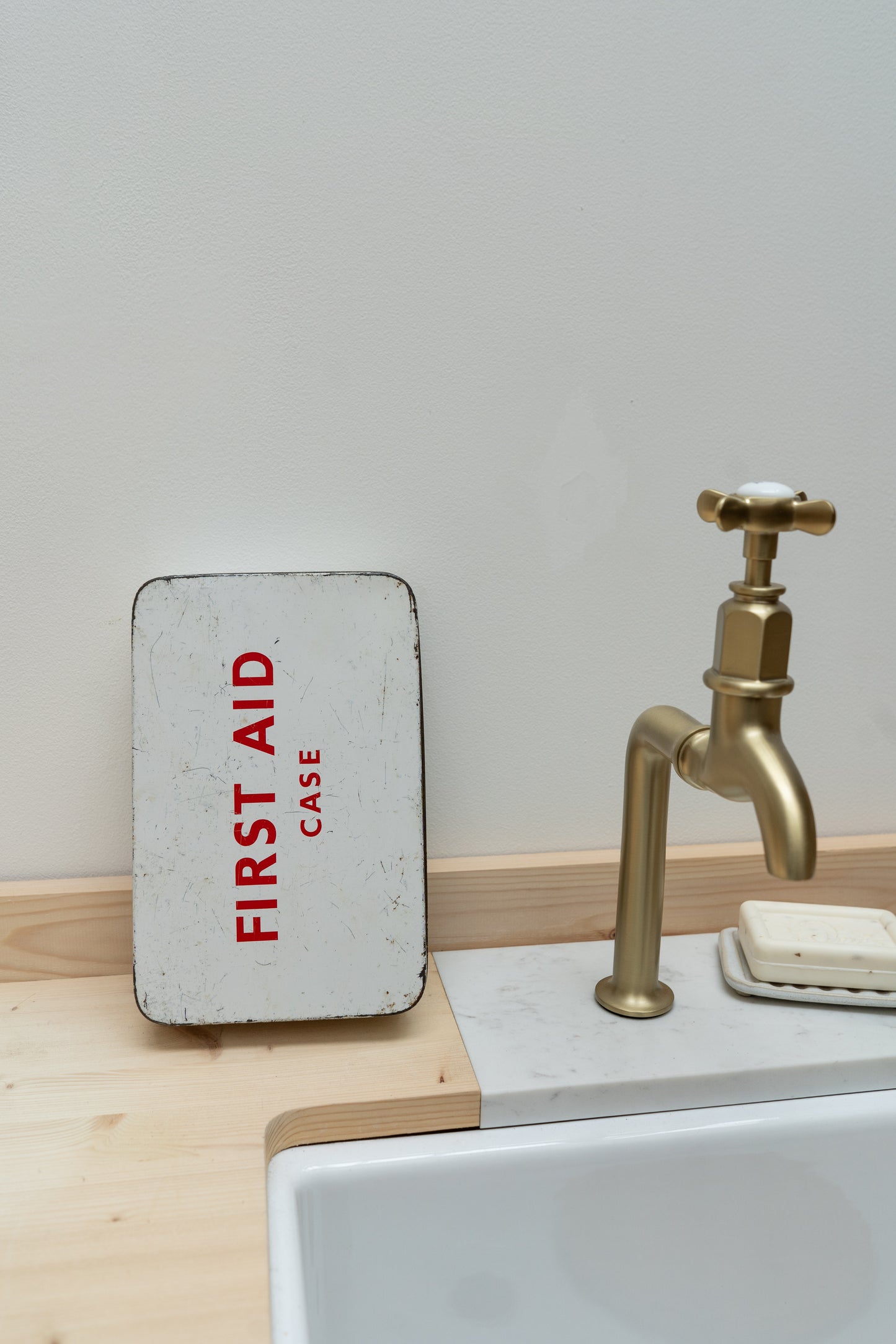 Small metal first aid case on a sink counter with a gold faucet in the background.