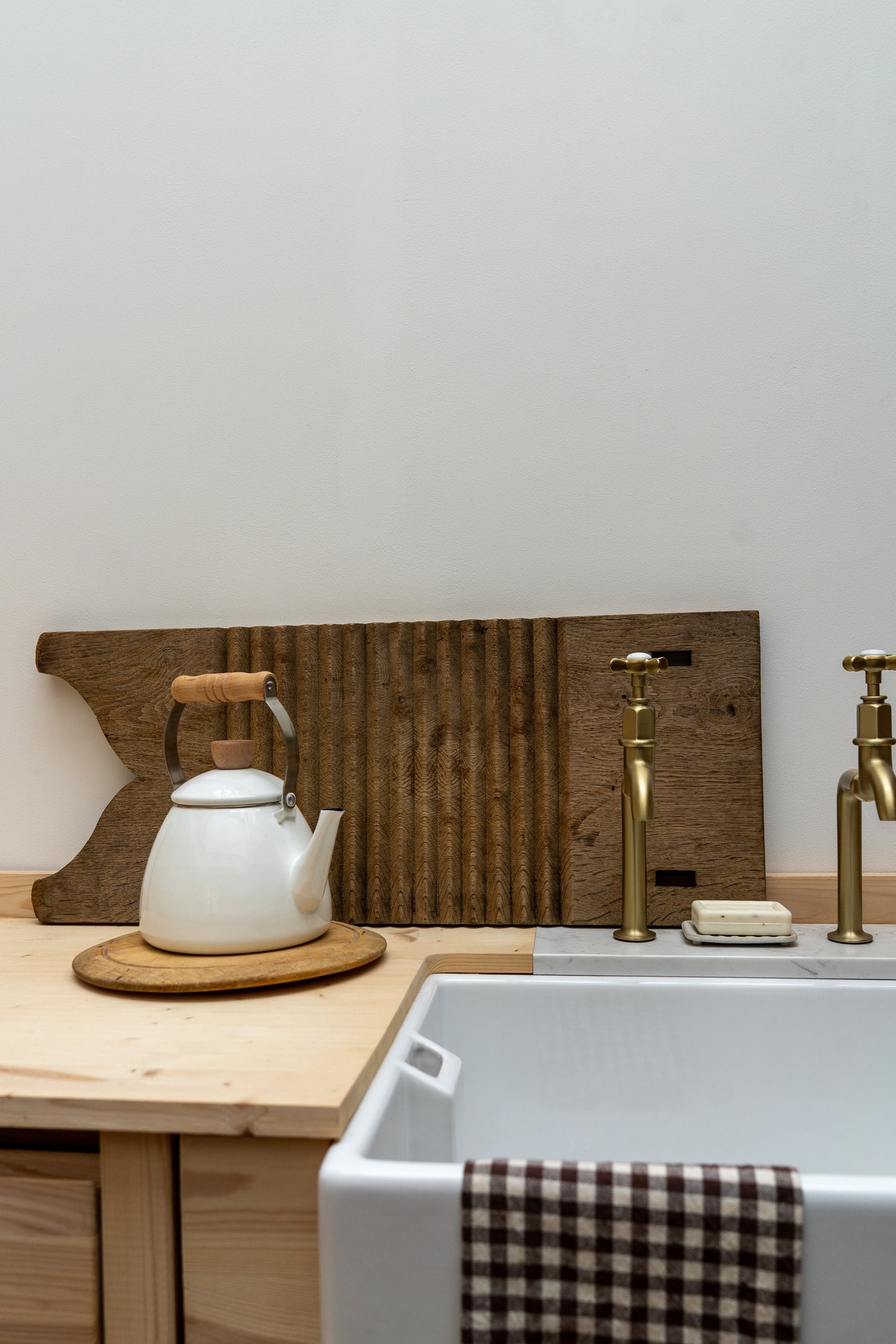 Kitchen setup with a white teapot on a wooden surface, a cutting board, and a sink with gold fixtures.