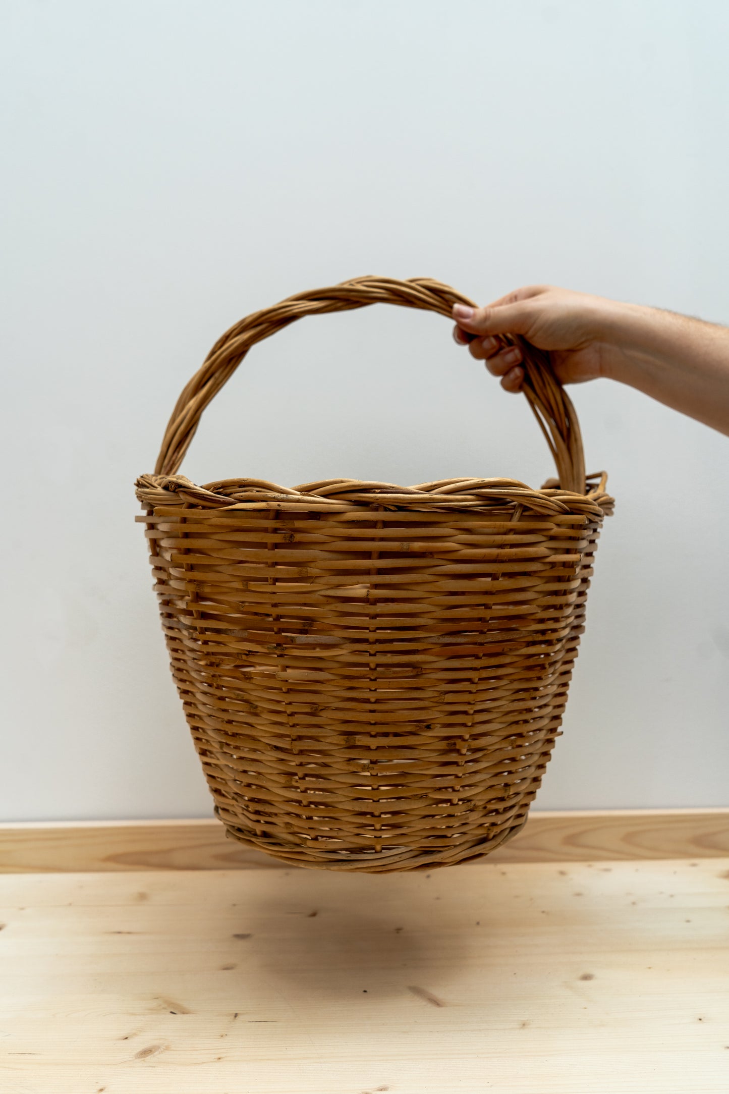 Hand holding a woven basket on a wooden surface with a white background