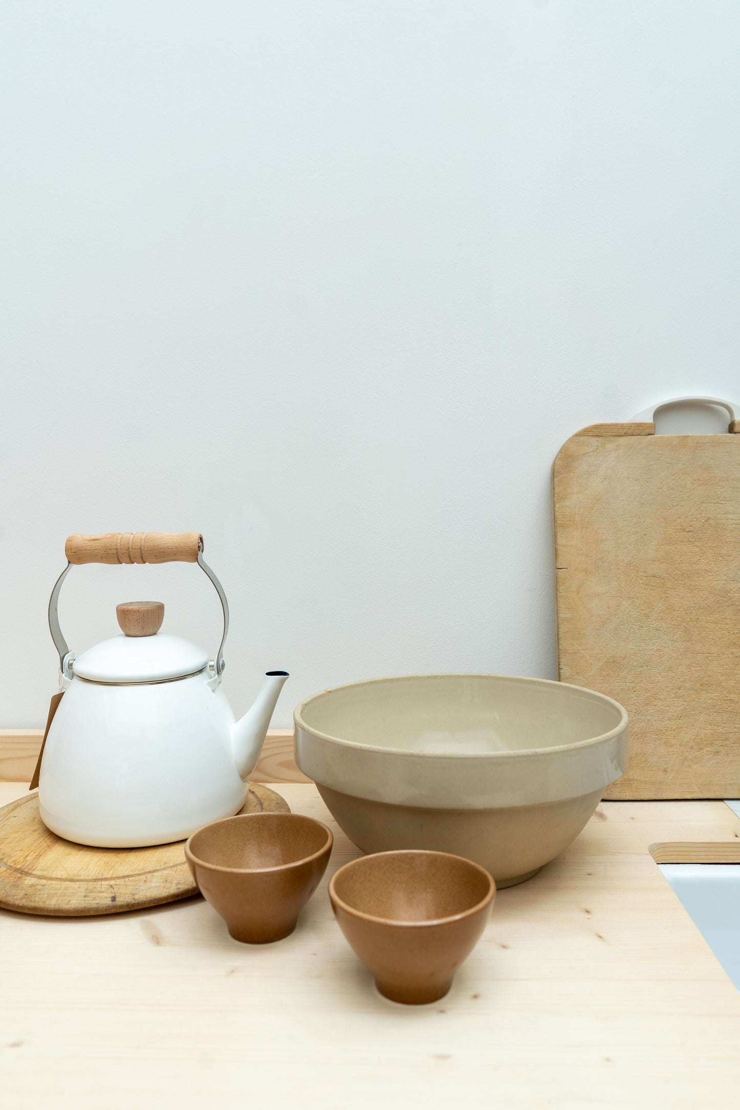 Ceramic teapot, bowls, and cups on a wooden surface with a light background