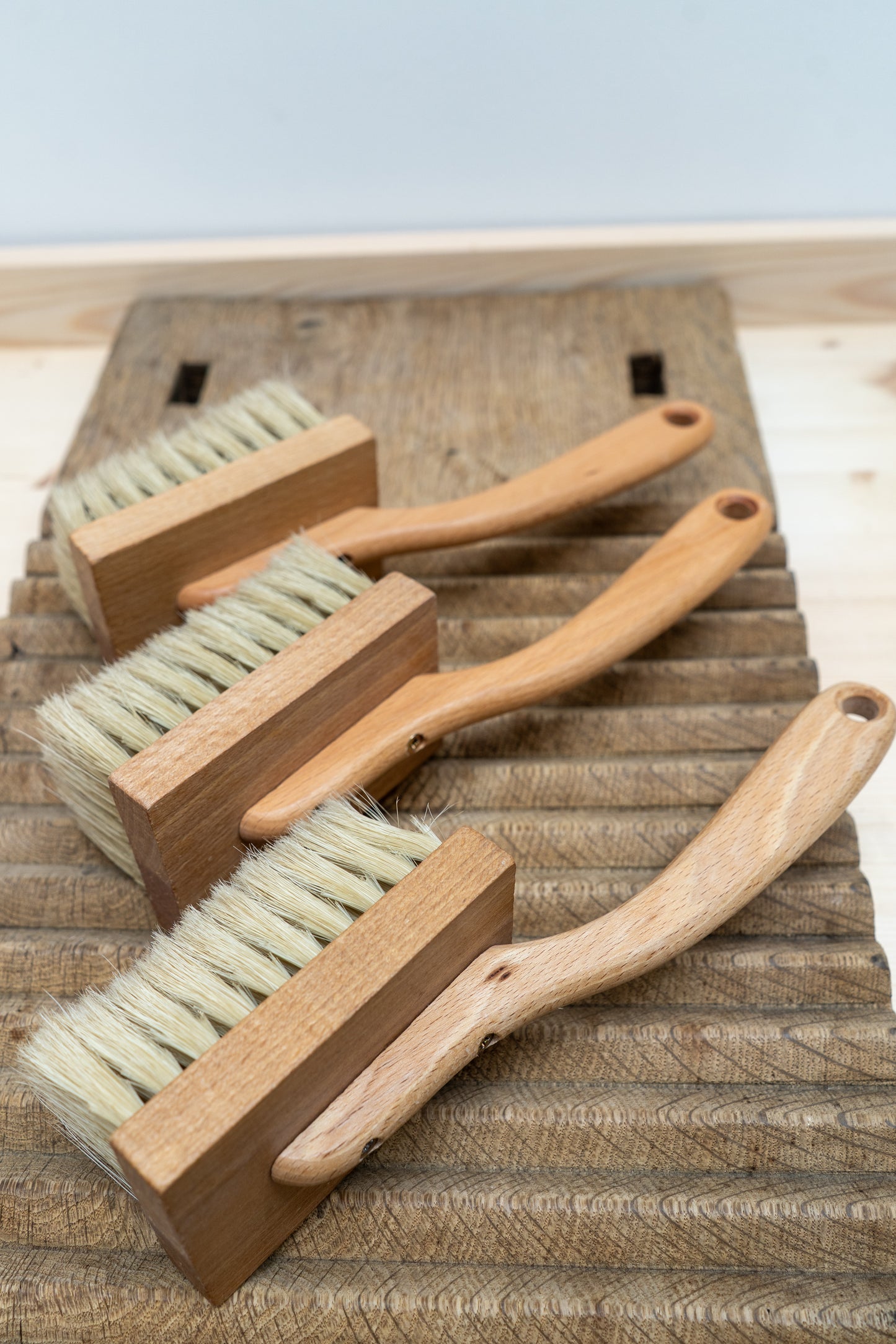 Three wooden brushes with bristle heads on a wooden surface.