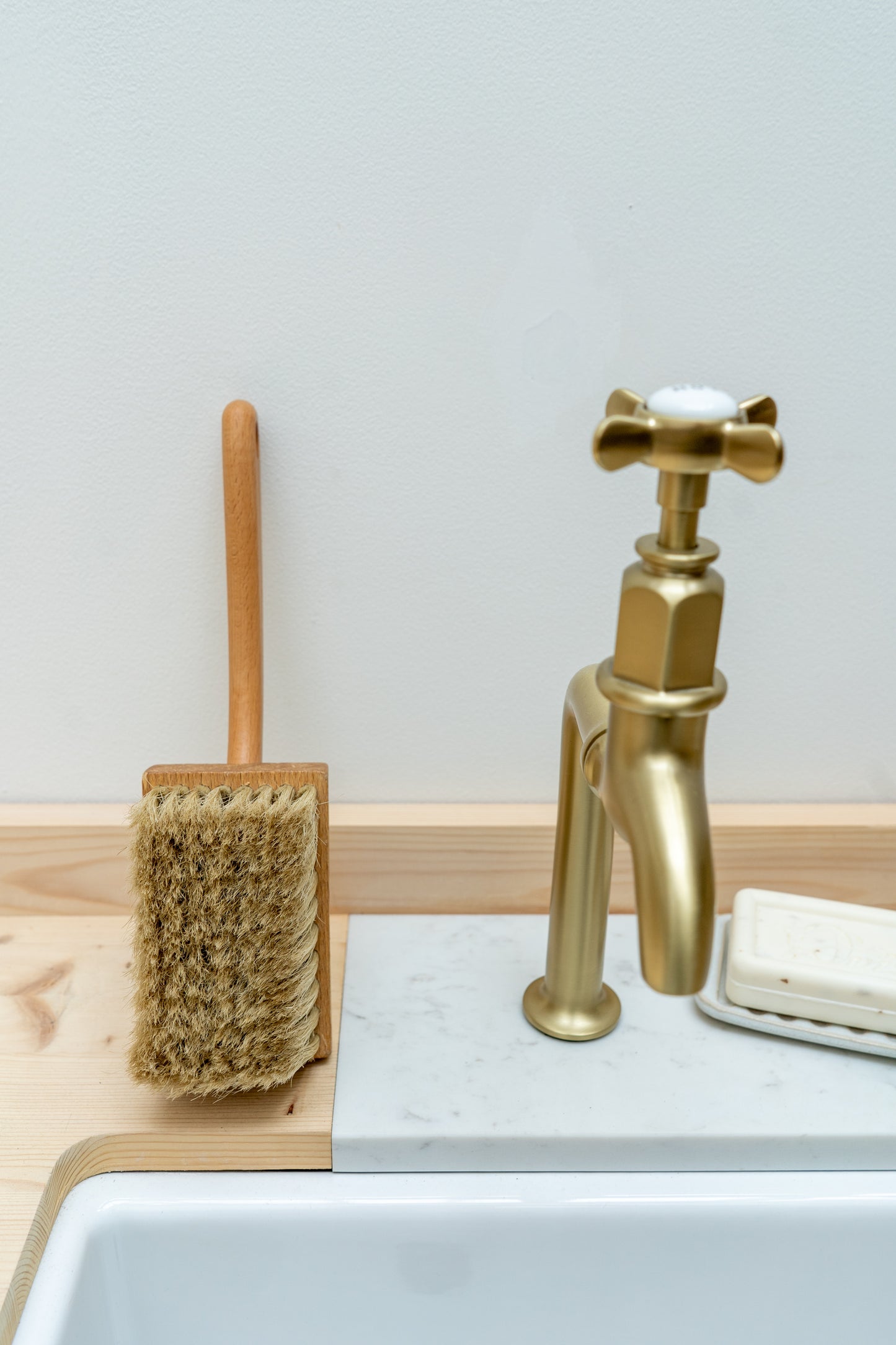 Gold faucet, scrub brush, and soap on a sink with a light gray background