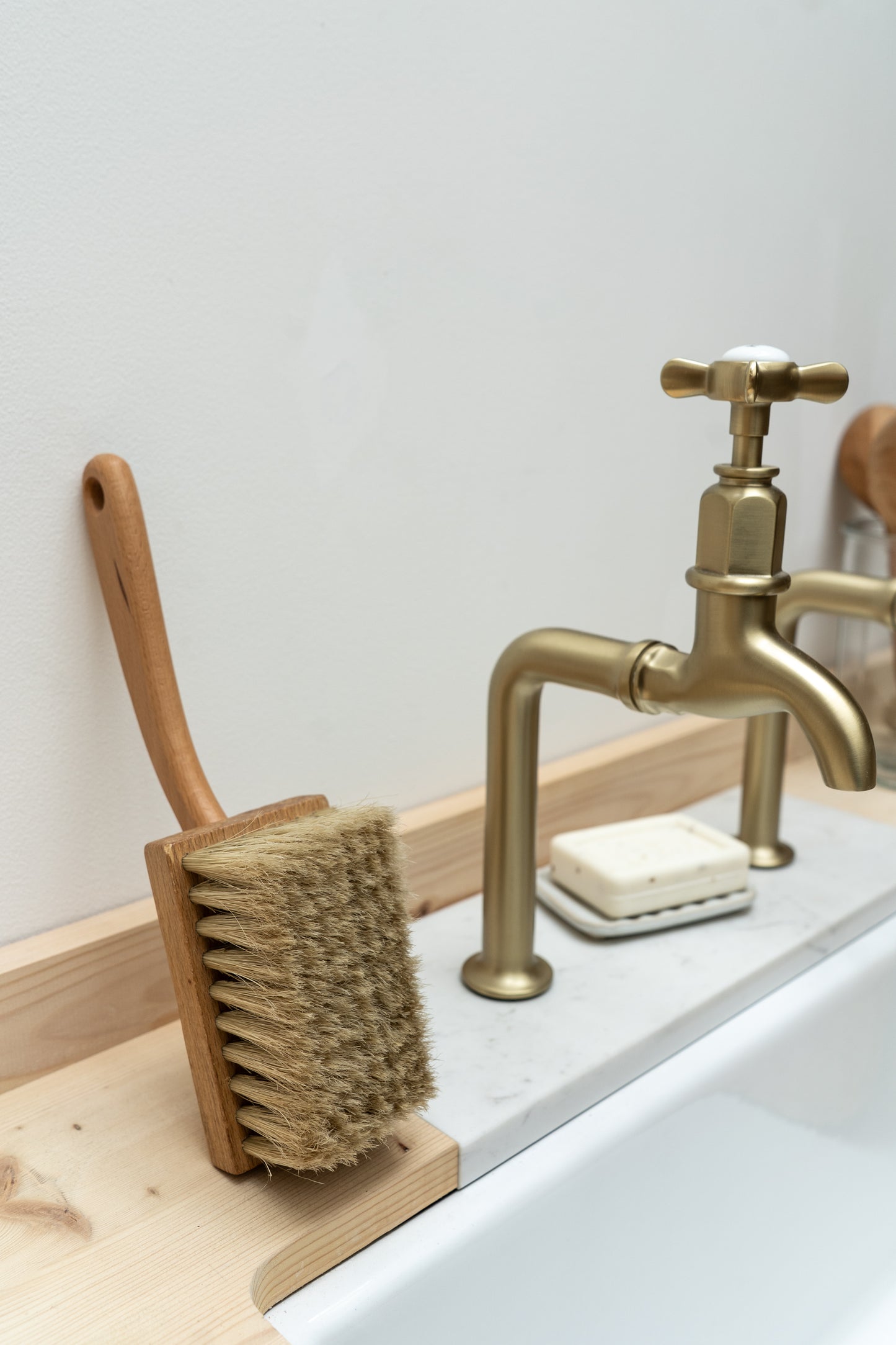 Bathroom setting with a gold faucet, scrub brush, and soap on a white countertop.