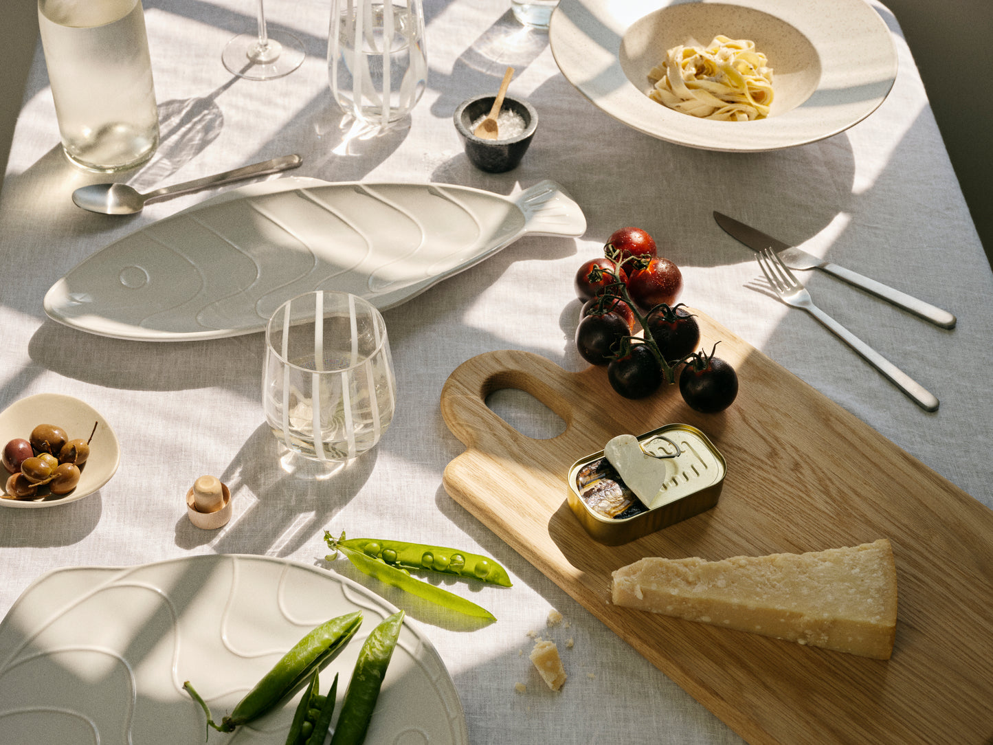 Table setting with cheese, grapes, and green beans on a wooden board.