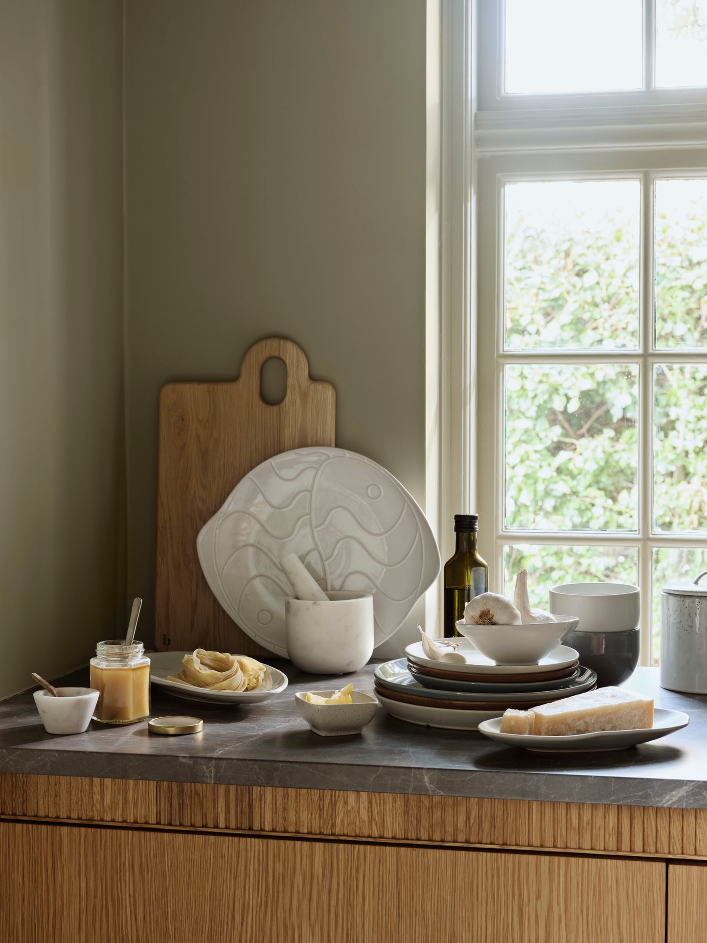 Kitchen worktop with ceramic plates, bowls, and a cutting board on a wooden table.
