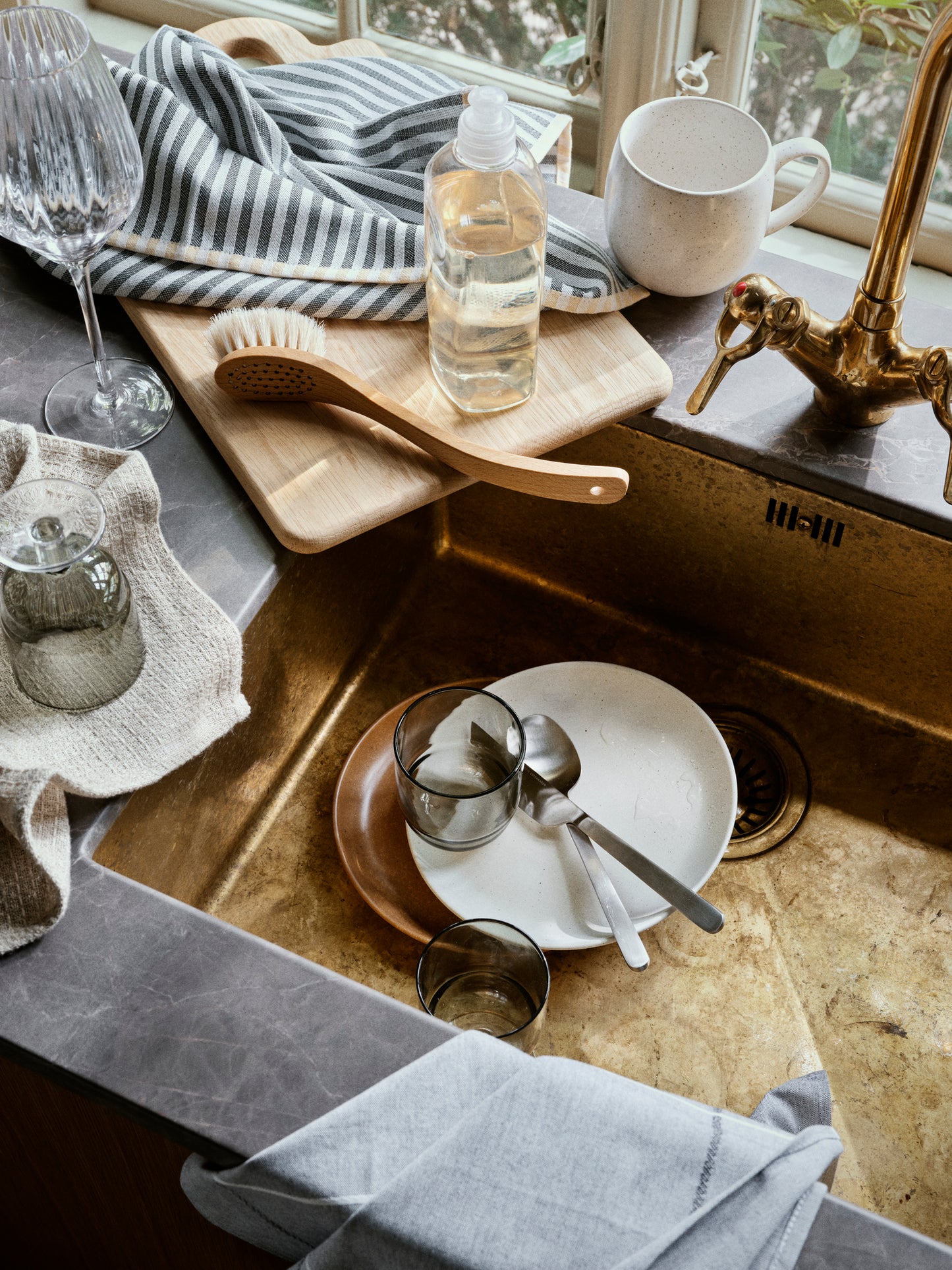 Brass kitchen sink, glasses, and kitchen items near a window.
