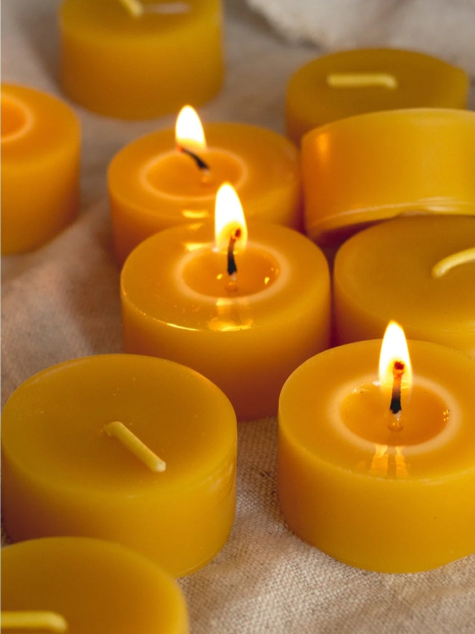 Multiple lit beeswax tealight candles on a textured surface.