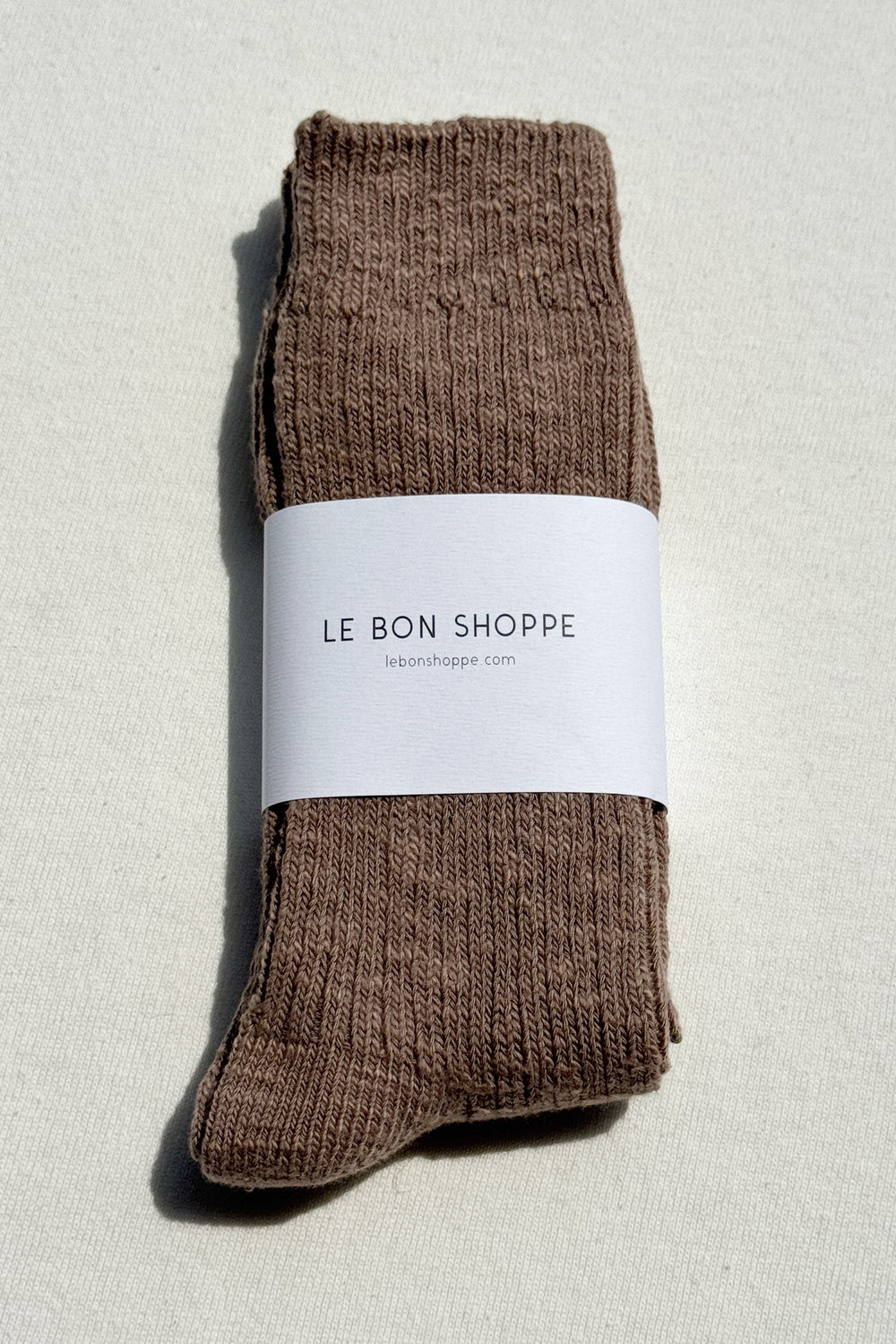 Le Bon Shoppe Cottage Socks in Flax folded with branded paper band on linen background