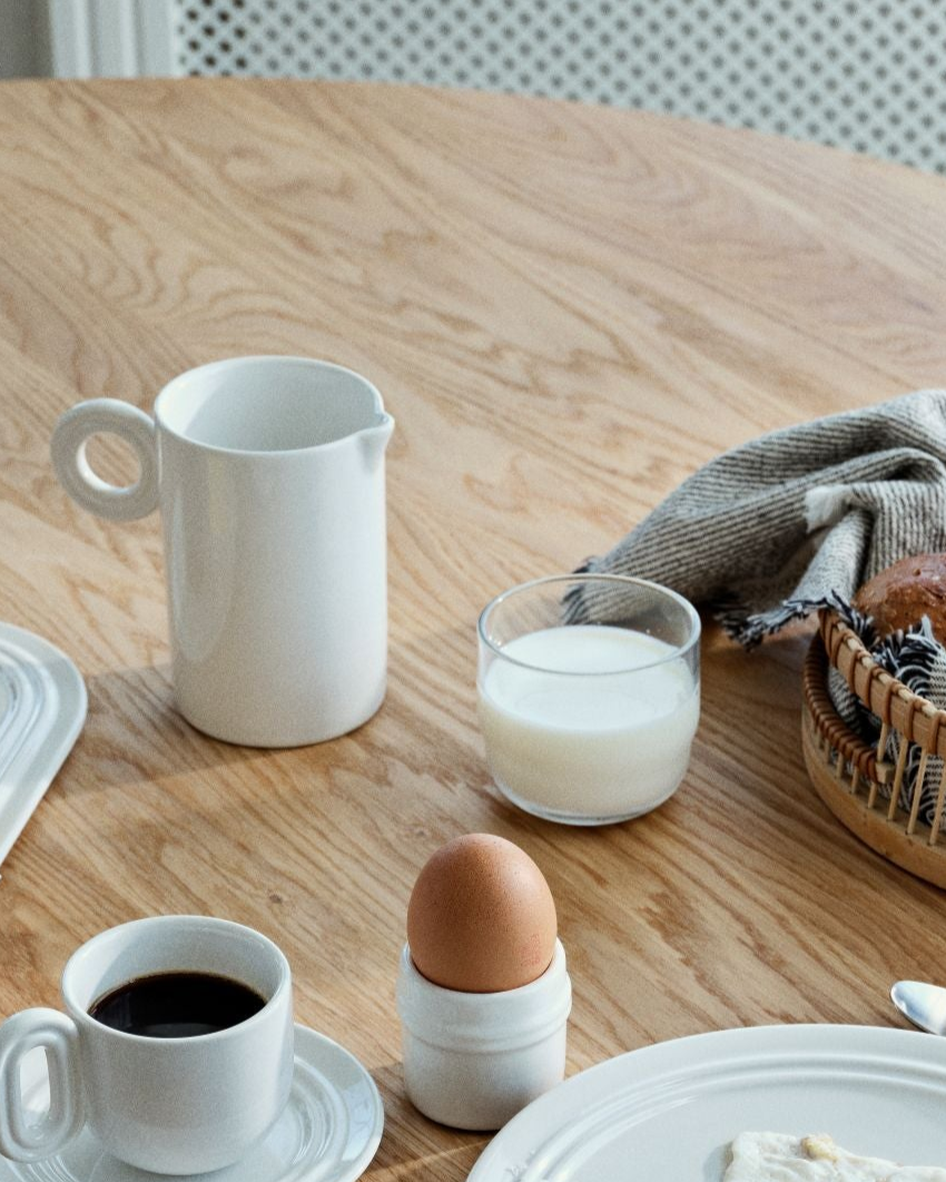 Breakfast setting with a white mug, glass of milk, and brown egg on a wooden table.