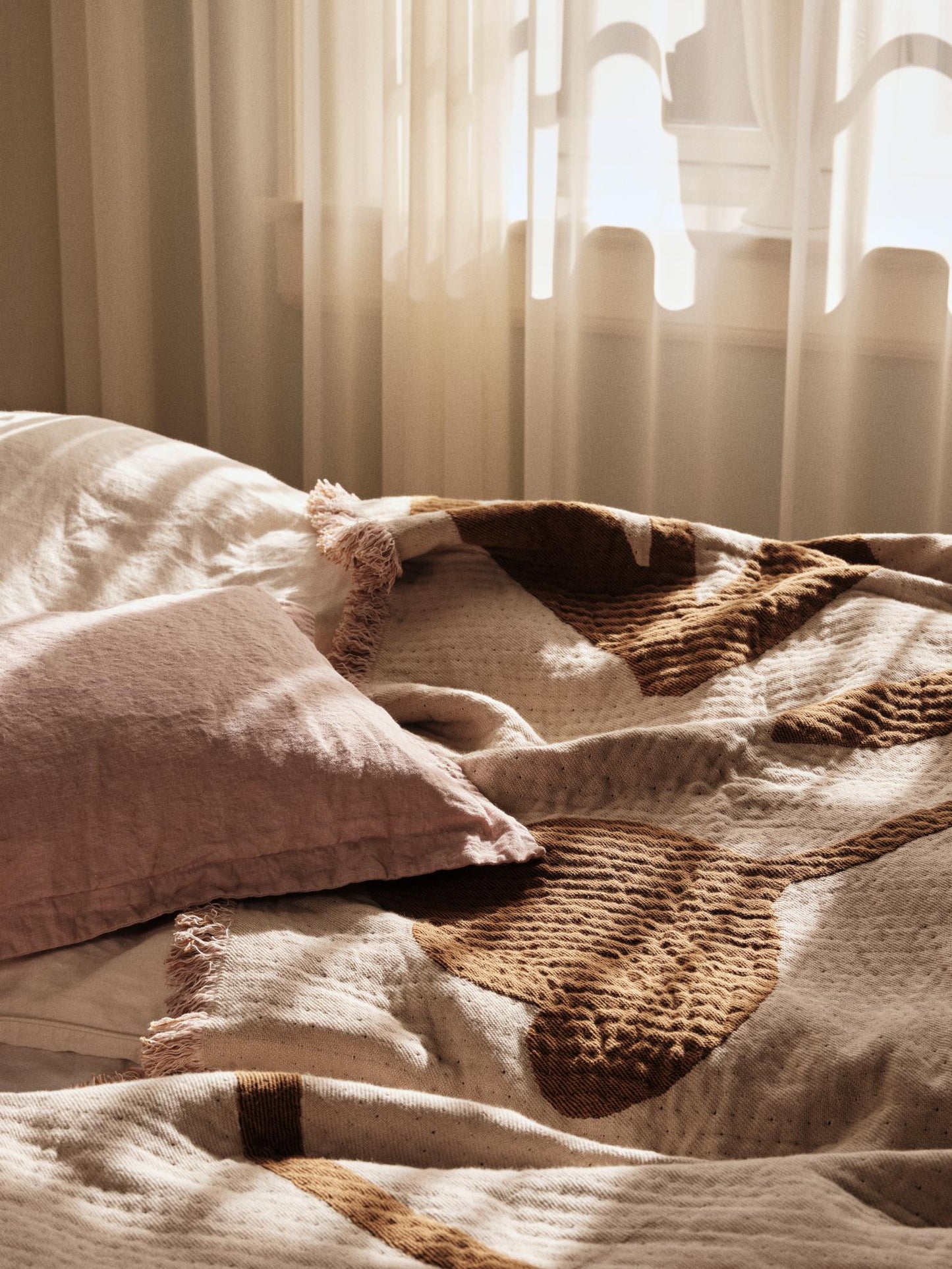 Cozy bedroom with textured bedding and pillows, soft lighting.