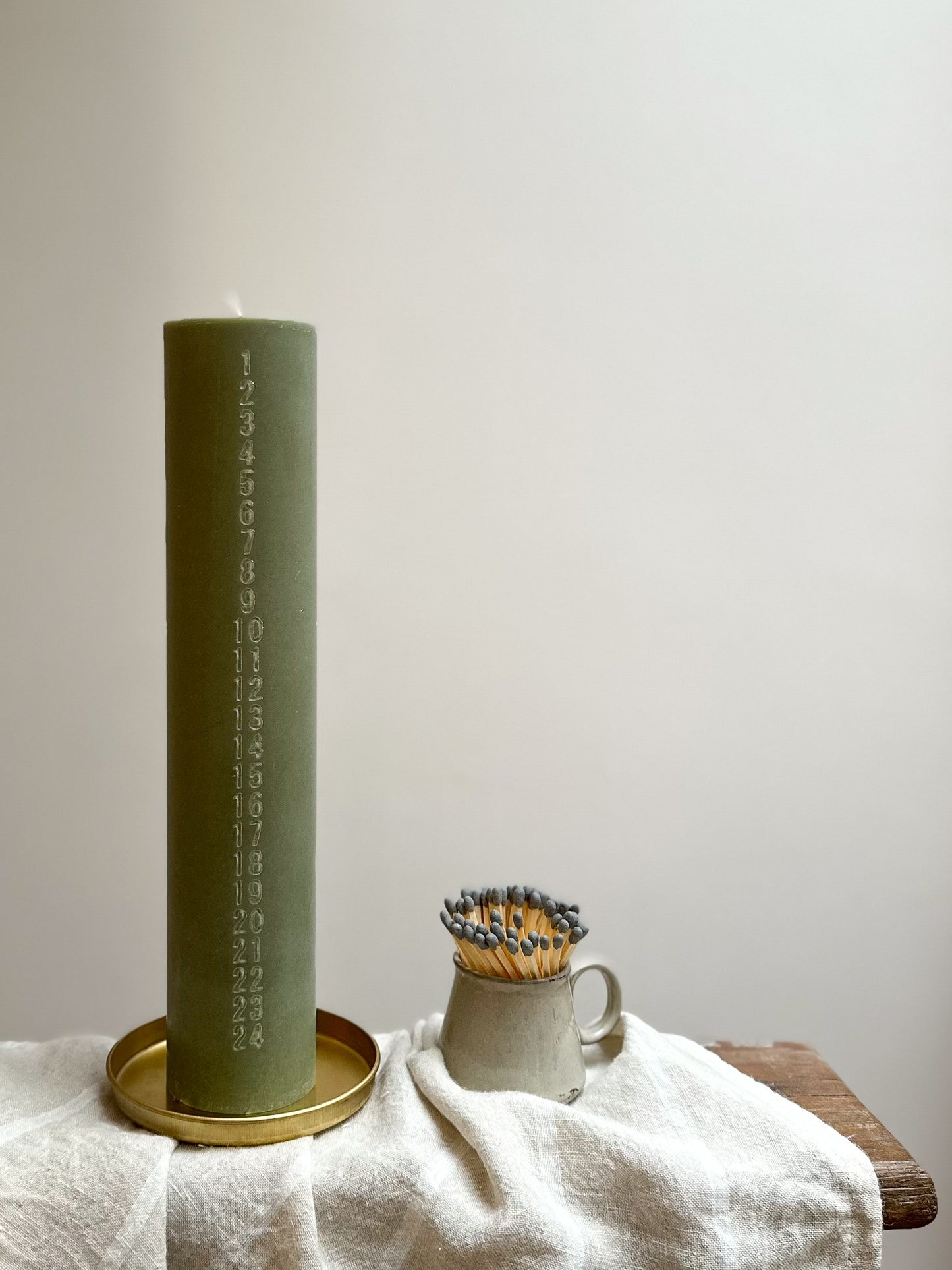 Green candle on a gold tray with a white cloth and wooden surface in the background