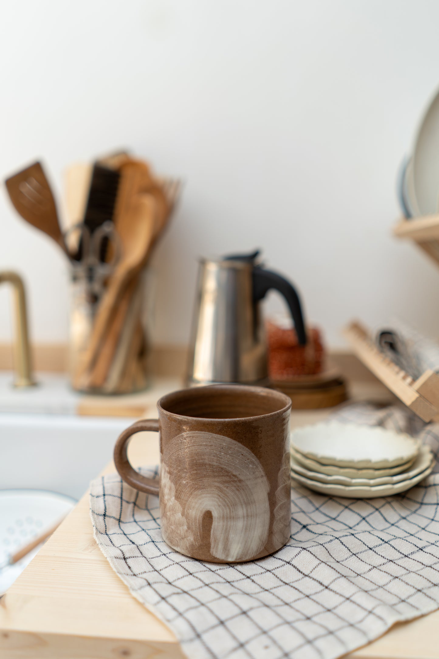 Brown ceramic mug on a kitchen counter with utensils and plates in the background