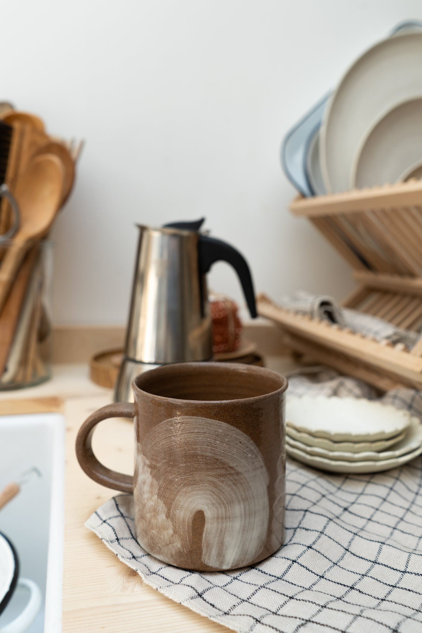 Brown ceramic mug on a kitchen counter with a dish rack and kitchen utensils in the background.
