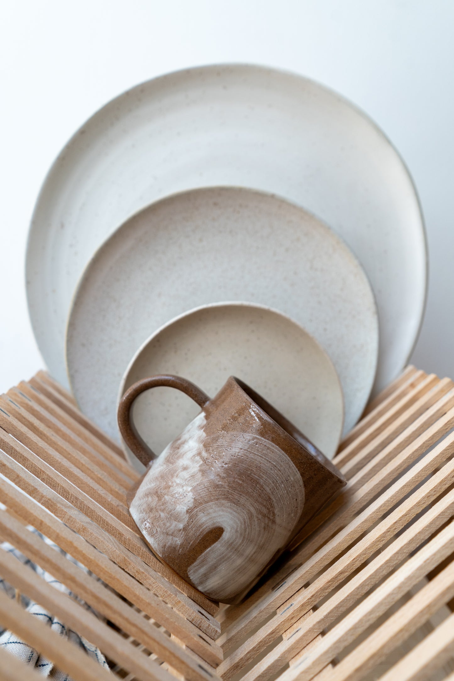 Ceramic dishes including a mug, plate, and bowl on a wooden surface with a light background