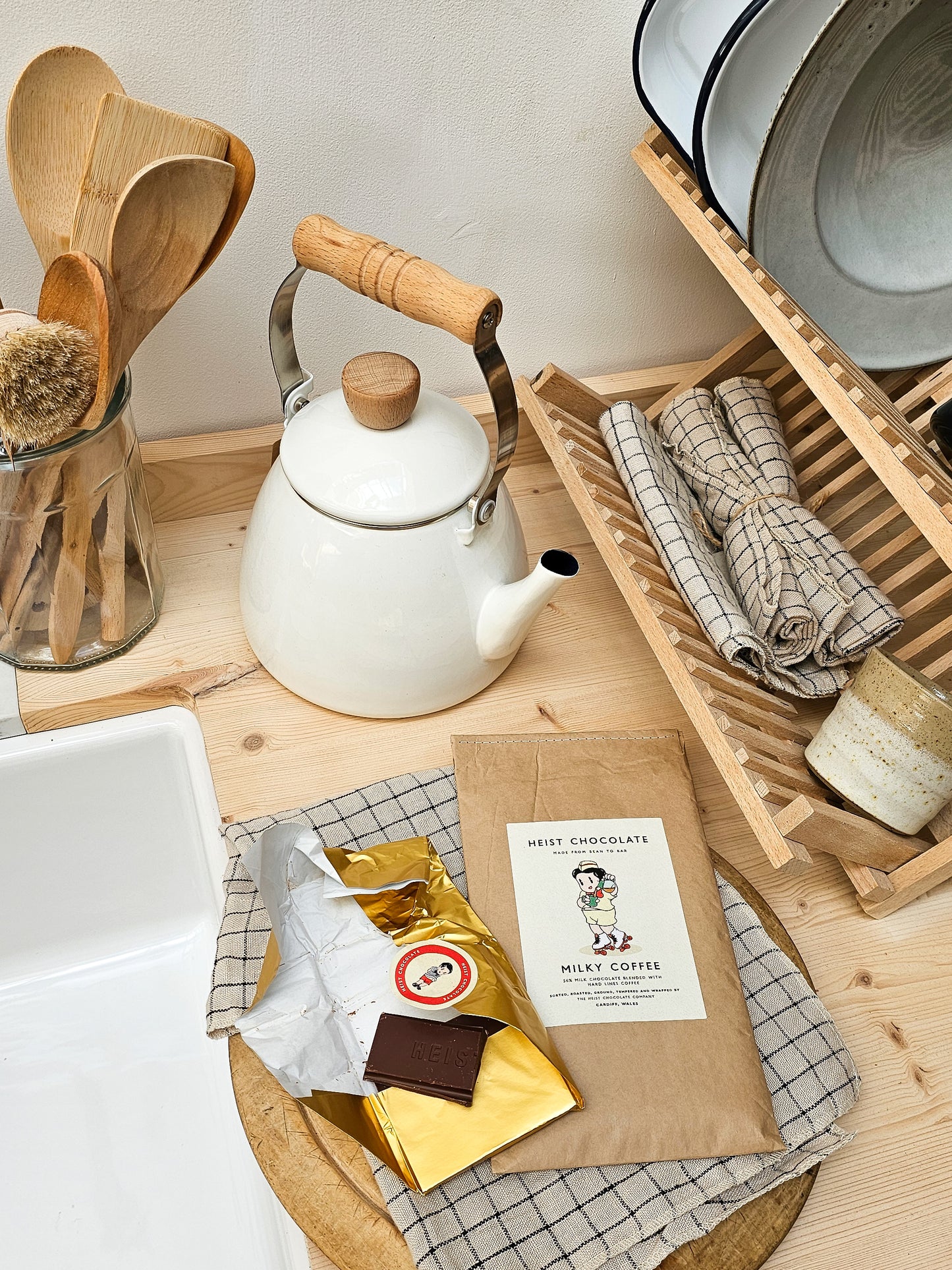 Kitchen counter with a white teapot, wooden utensils, and chocolate packaging.