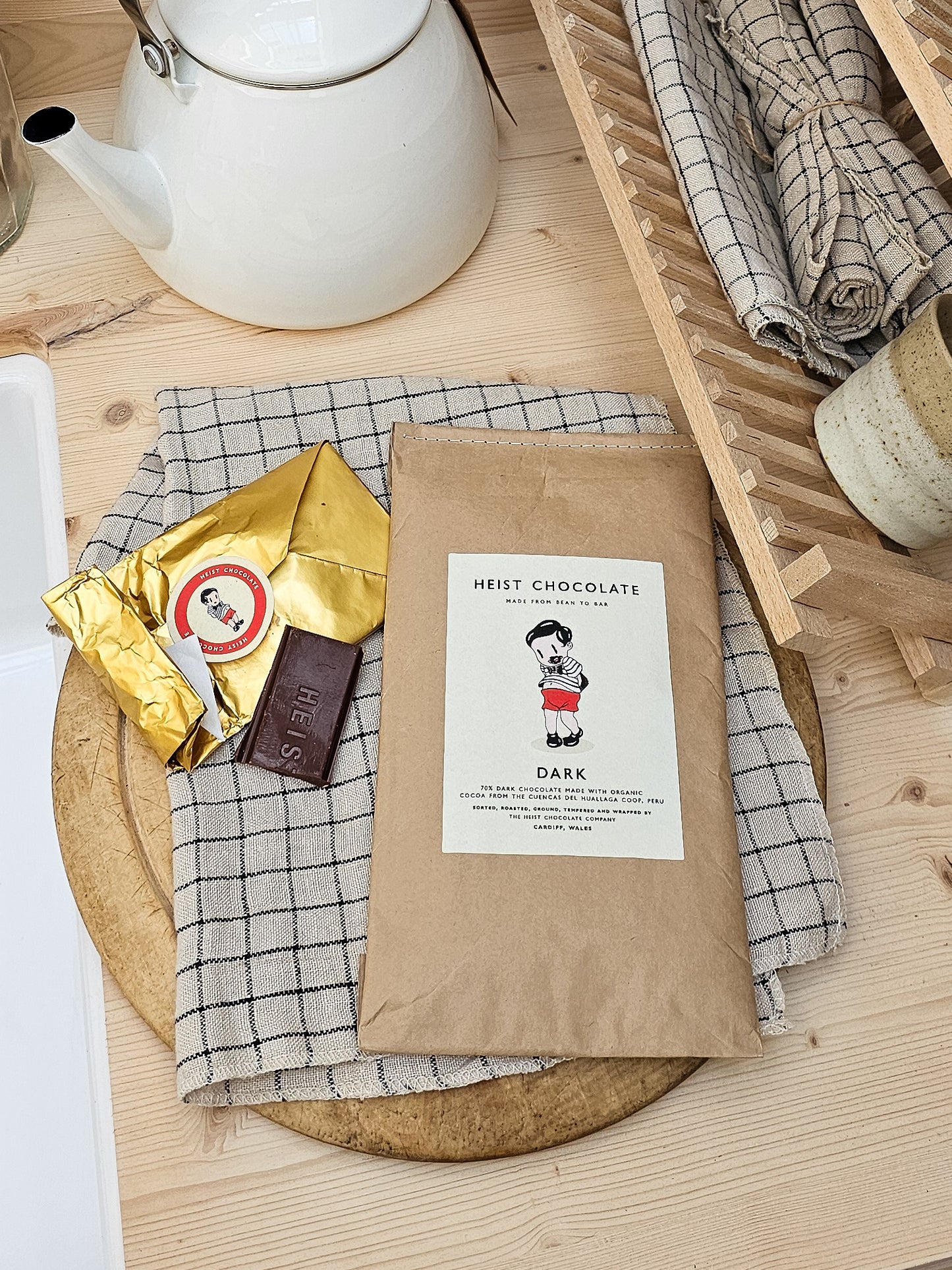 Heist Chocolate packaging on a wooden surface with plaid cloth and teapot.