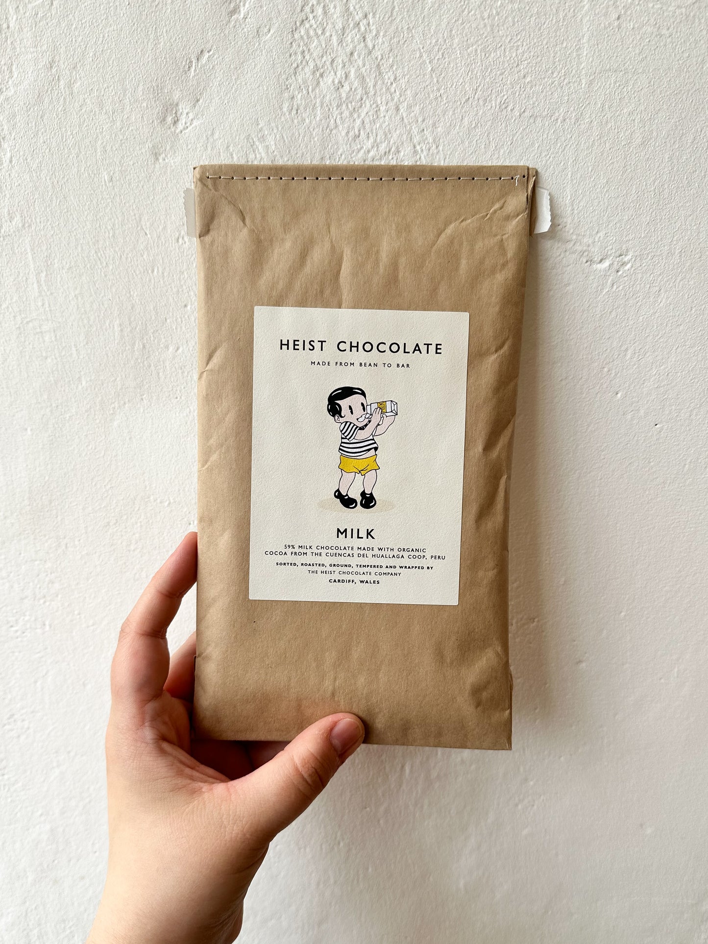 A hand holding a Heist Chocolate bar with '59% Milk' text on the packaging, against a neutral background.