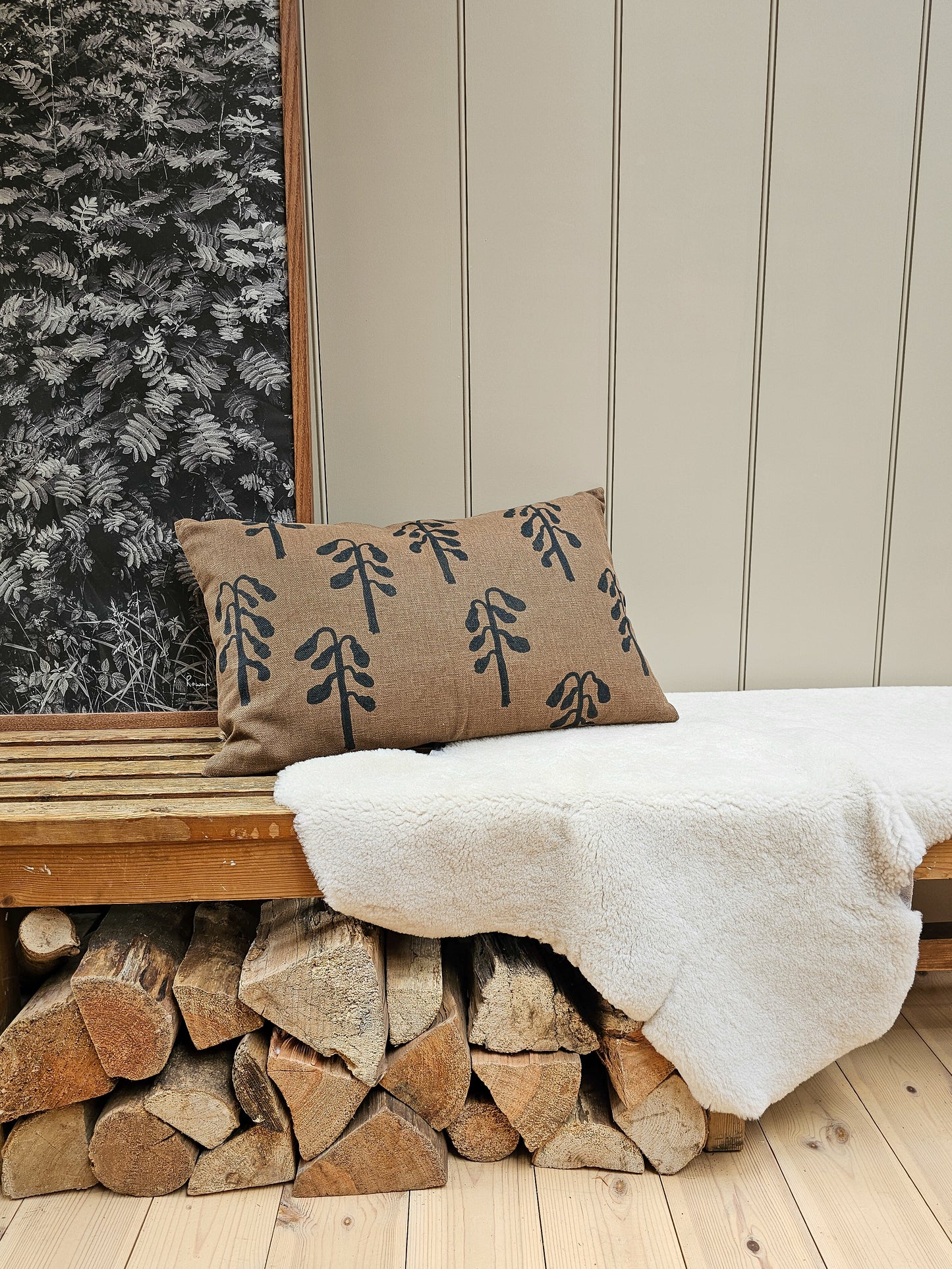 Wooden bench with a decorative pillow and white sheepskin against a wall with vertical paneling.