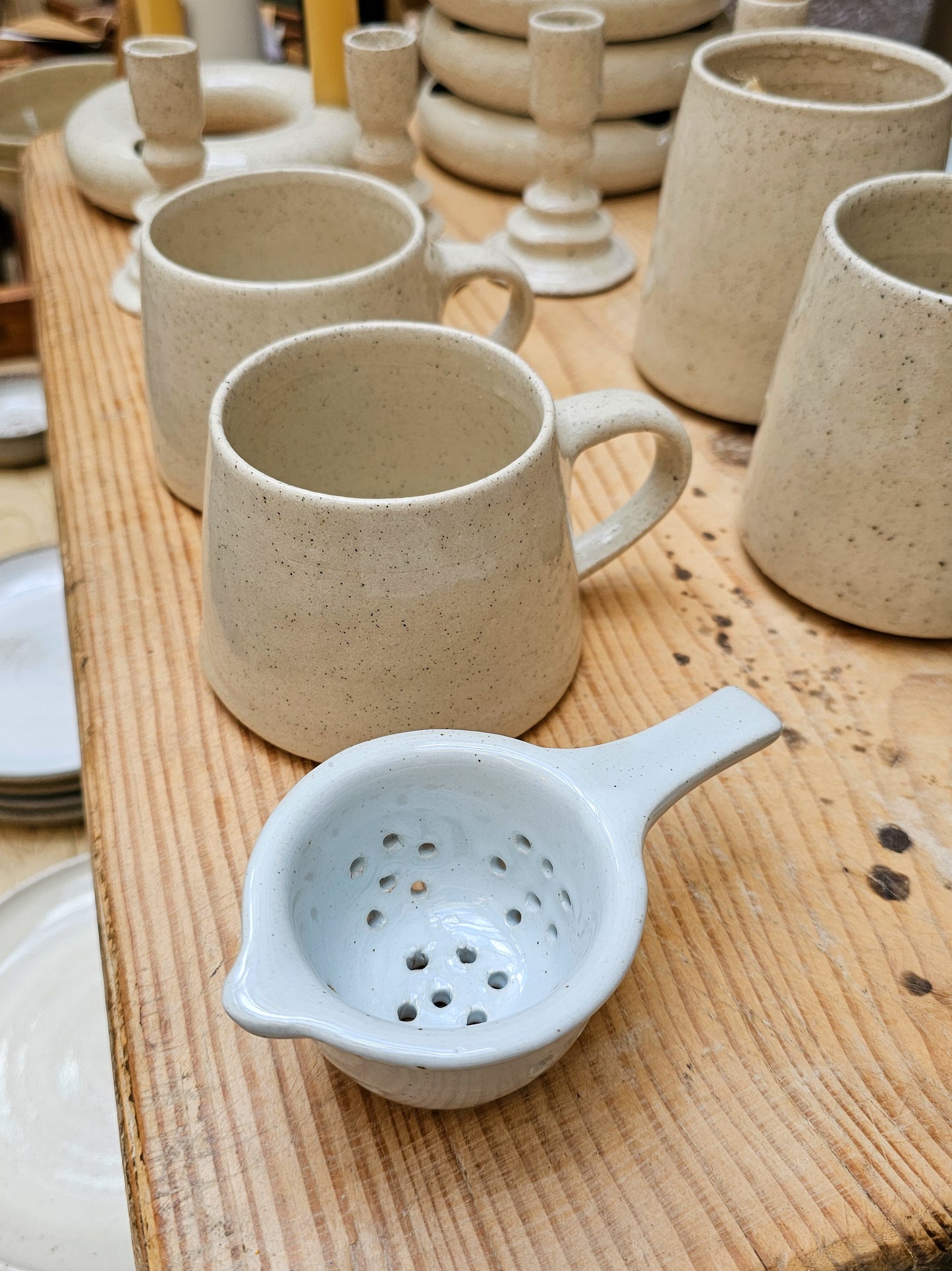 Ceramic mugs and a strainer on a wooden surface