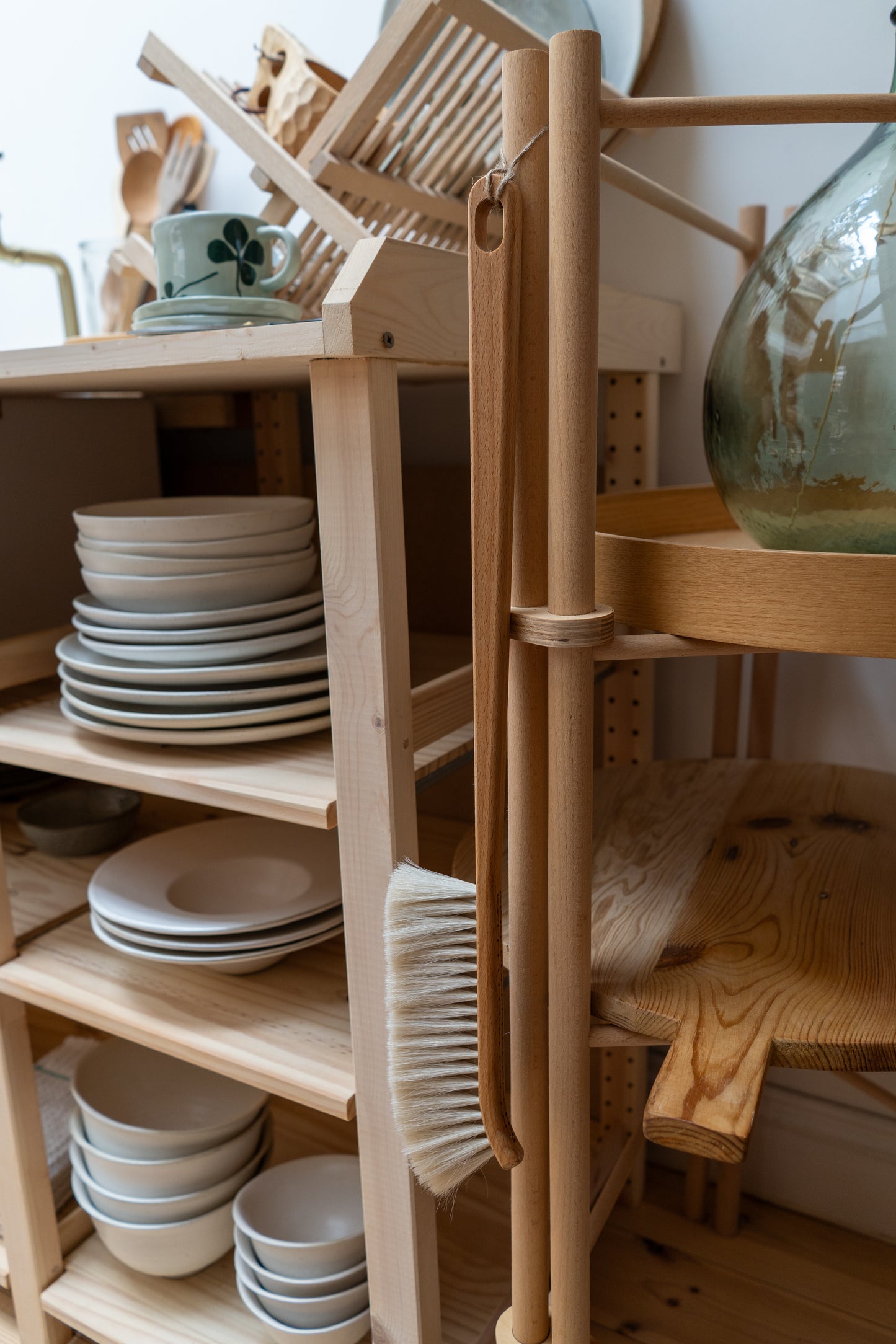Wooden kitchen shelf with plates, bowls, and a dust brush against a white wall.