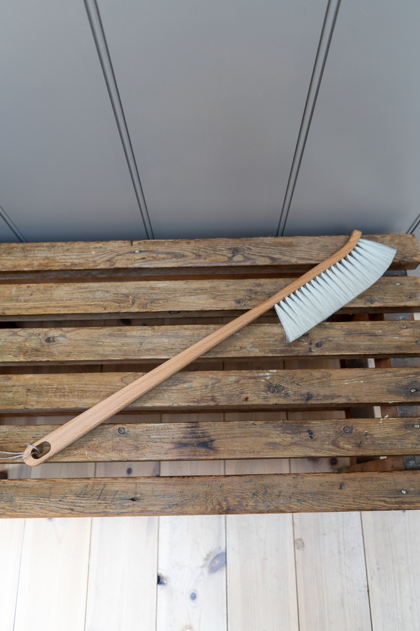 Dust brush with a white bristle head on a slatted bench.