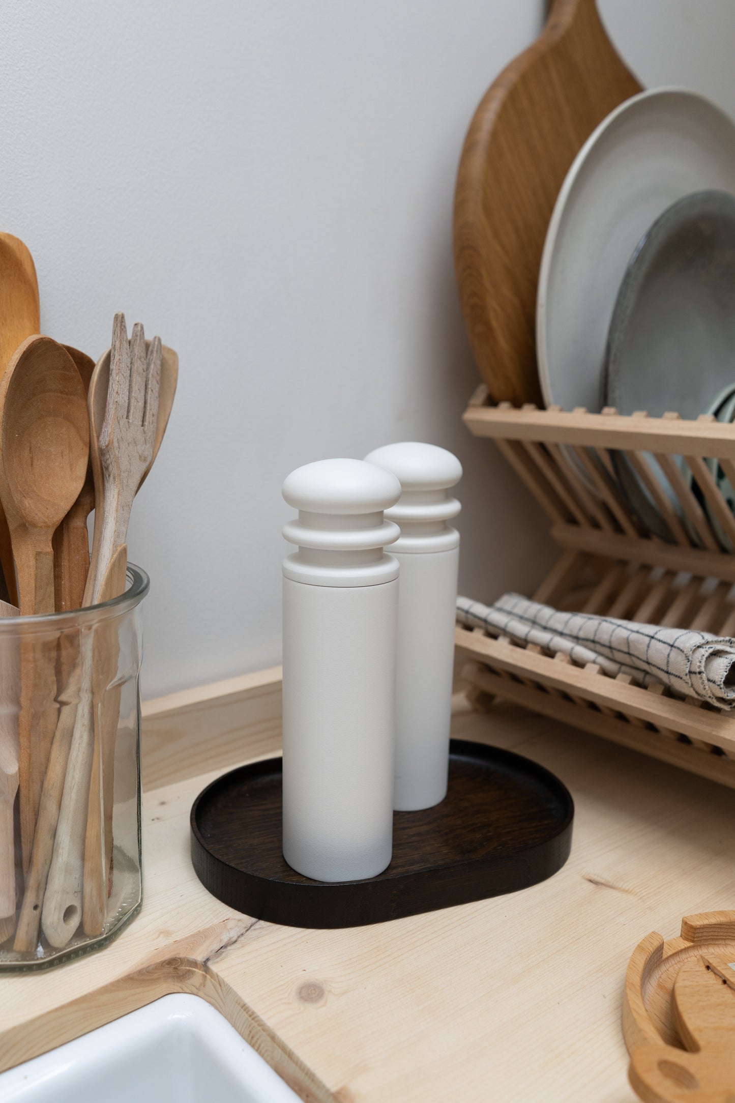 White salt and pepper shakers on a dark wooden coaster with a kitchen counter background.