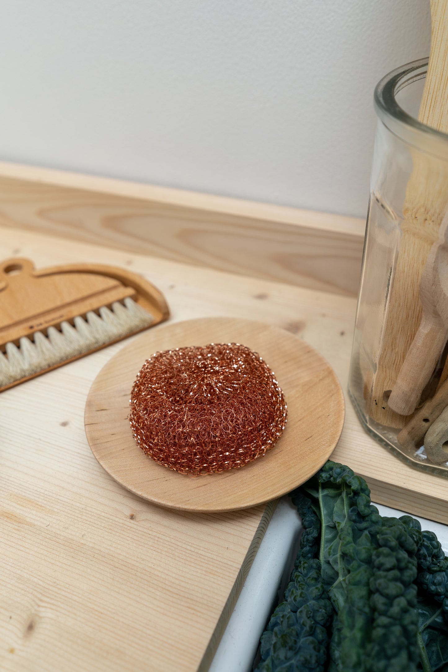 Brown scrubber on a wooden plate with a brush and glass container in the background.