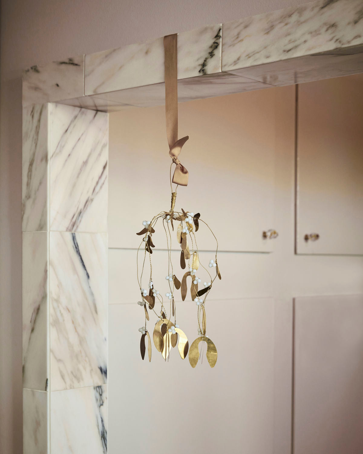 A brass mistletoe ornament hanging from a marble-tiled wall, featuring intricate leaves and berries.