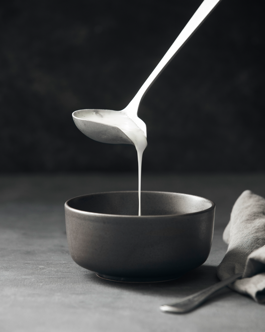 Spoon pouring a white liquid into a dark bowl on a dark background