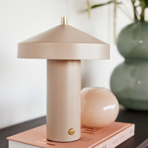 A clay-colored, modern style LED table lamp with a round shade and a cylindrical base, placed on a book on a table.