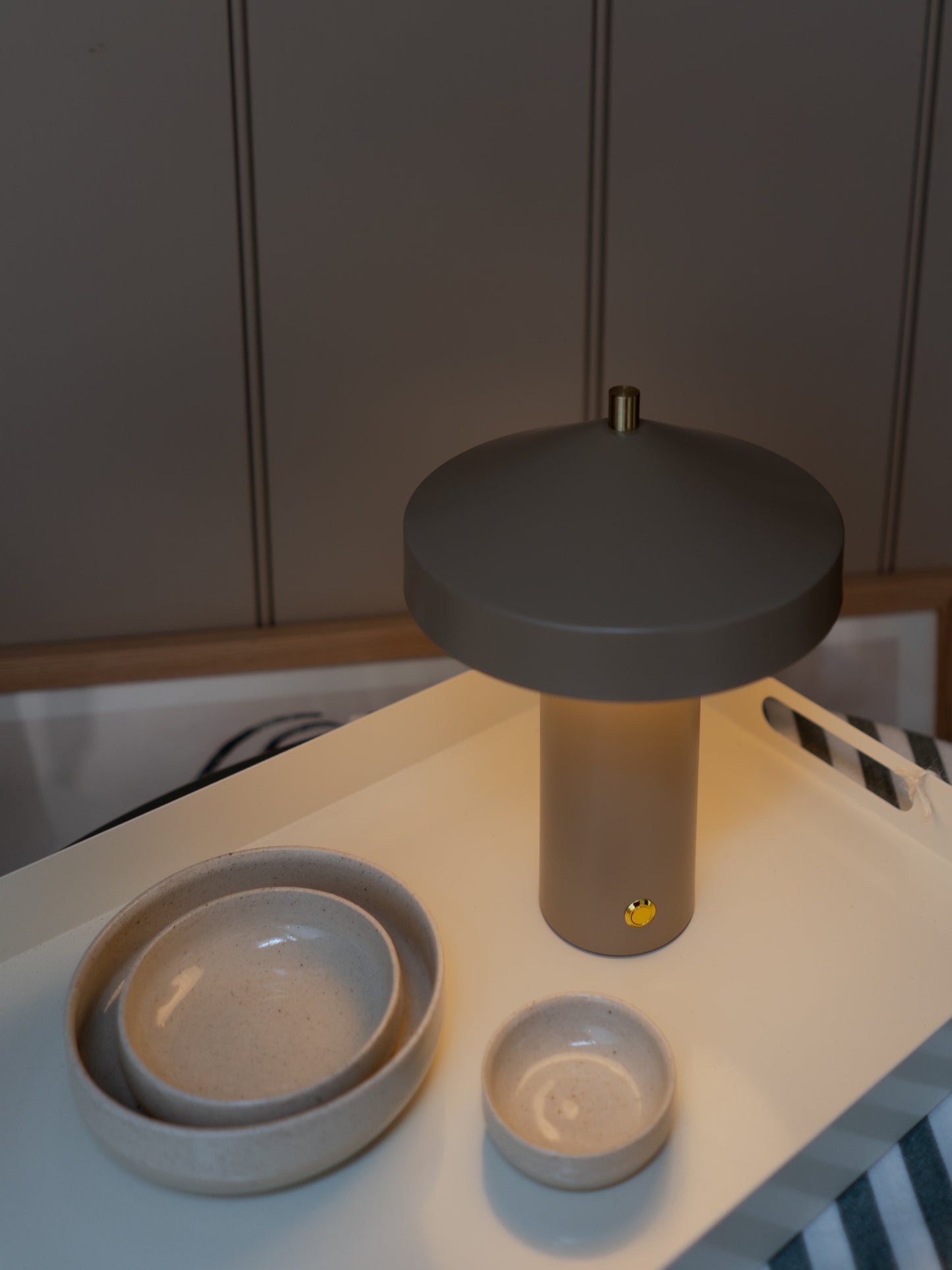 Beige rechargeable lamp on a white tray with ceramic bowls below.