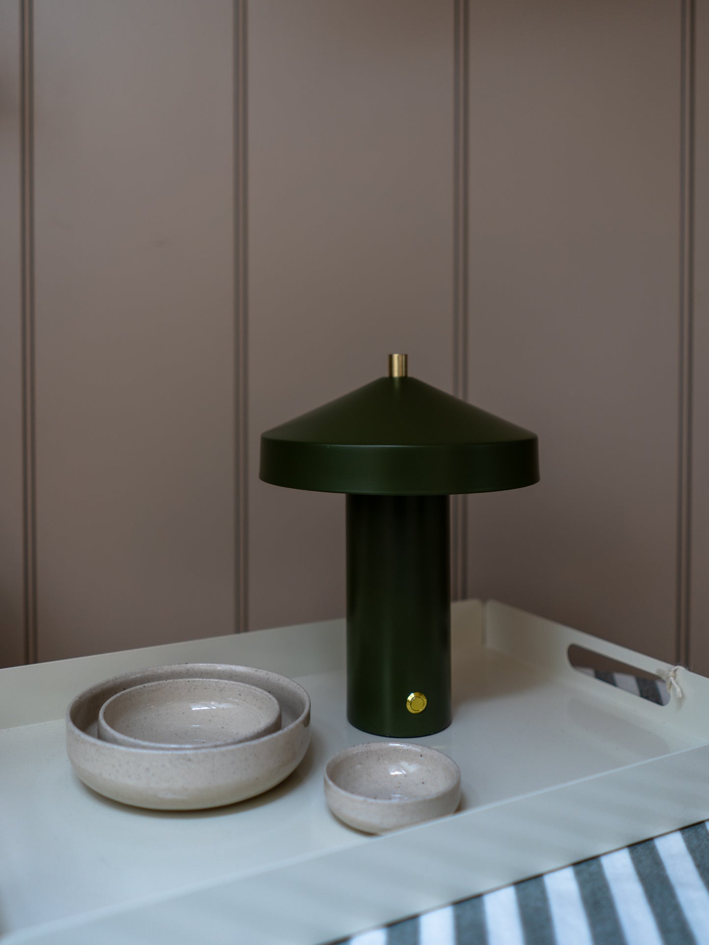 Green lamp and ceramic bowls on a white surface with a striped fabric background
