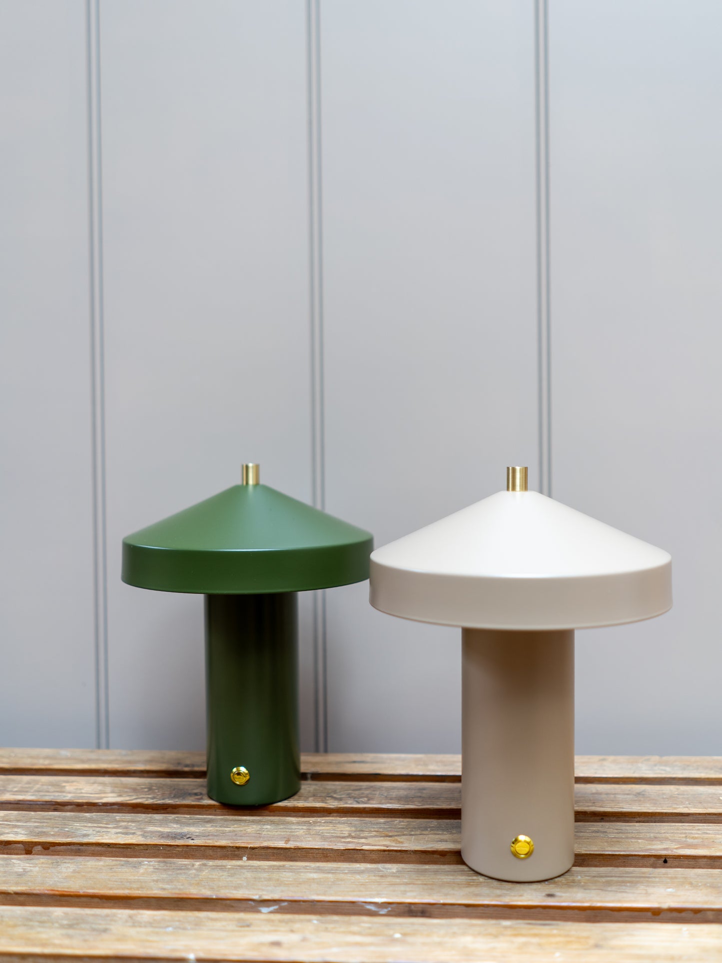 Two table lamps, one green and one beige, on a wooden surface with a gray paneled wall background.