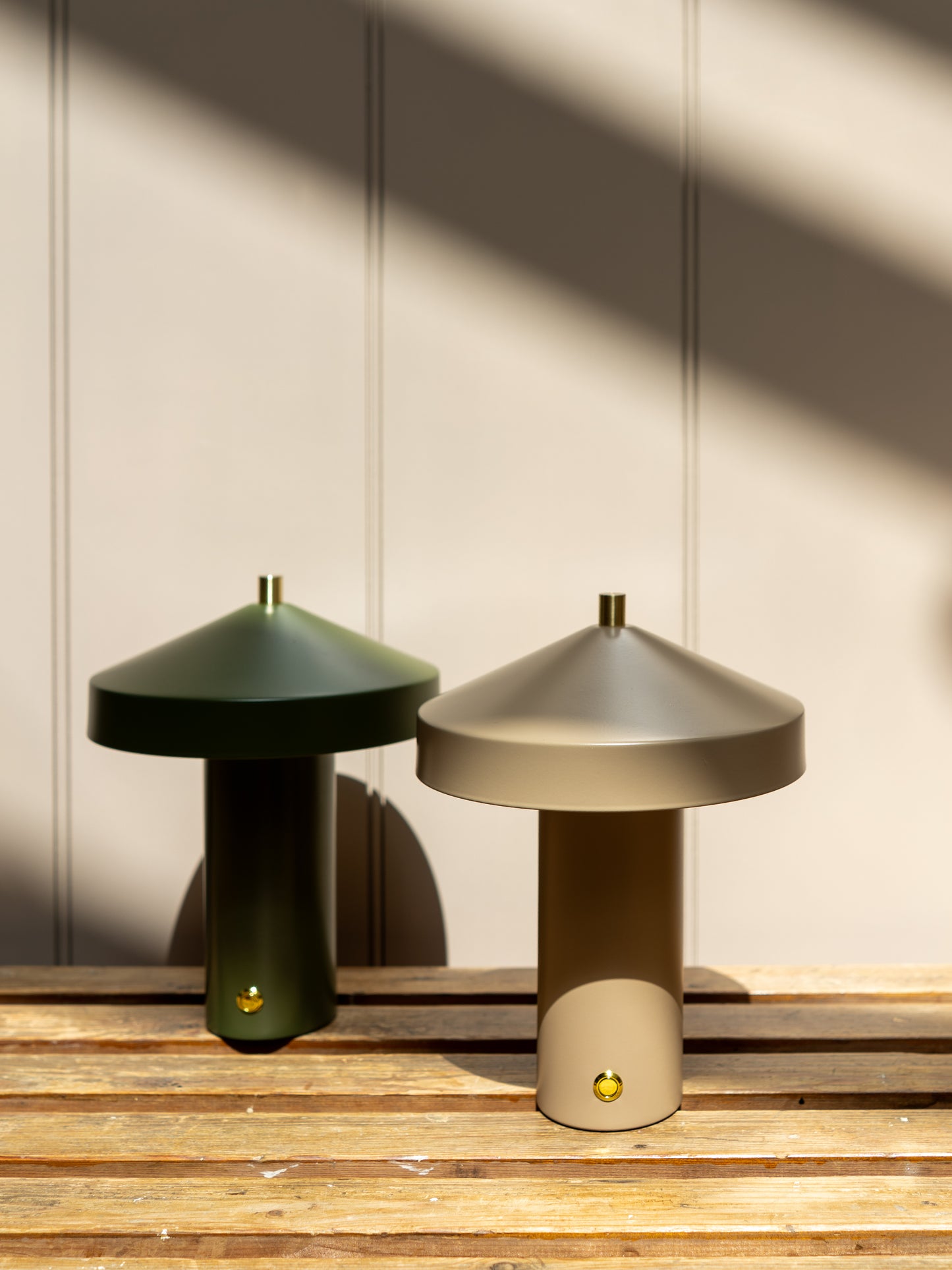 Two wireless lamps, one green and one beige, on a wooden surface with a neutral wall background.