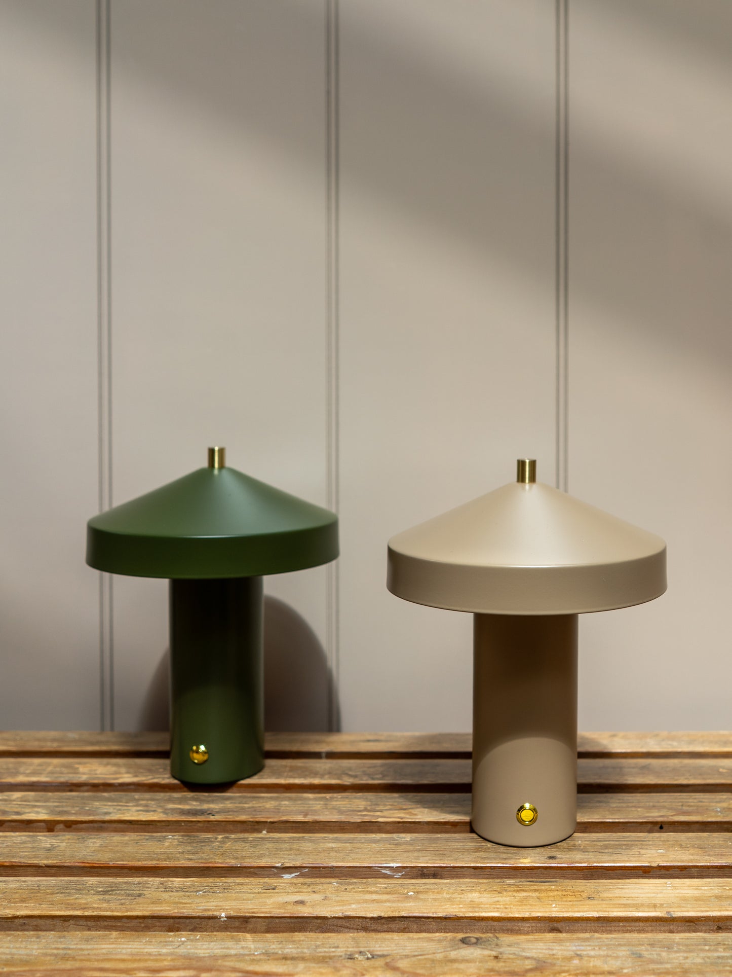 Two modern table lamps, one green and one beige, on a wooden surface with a neutral wall background.