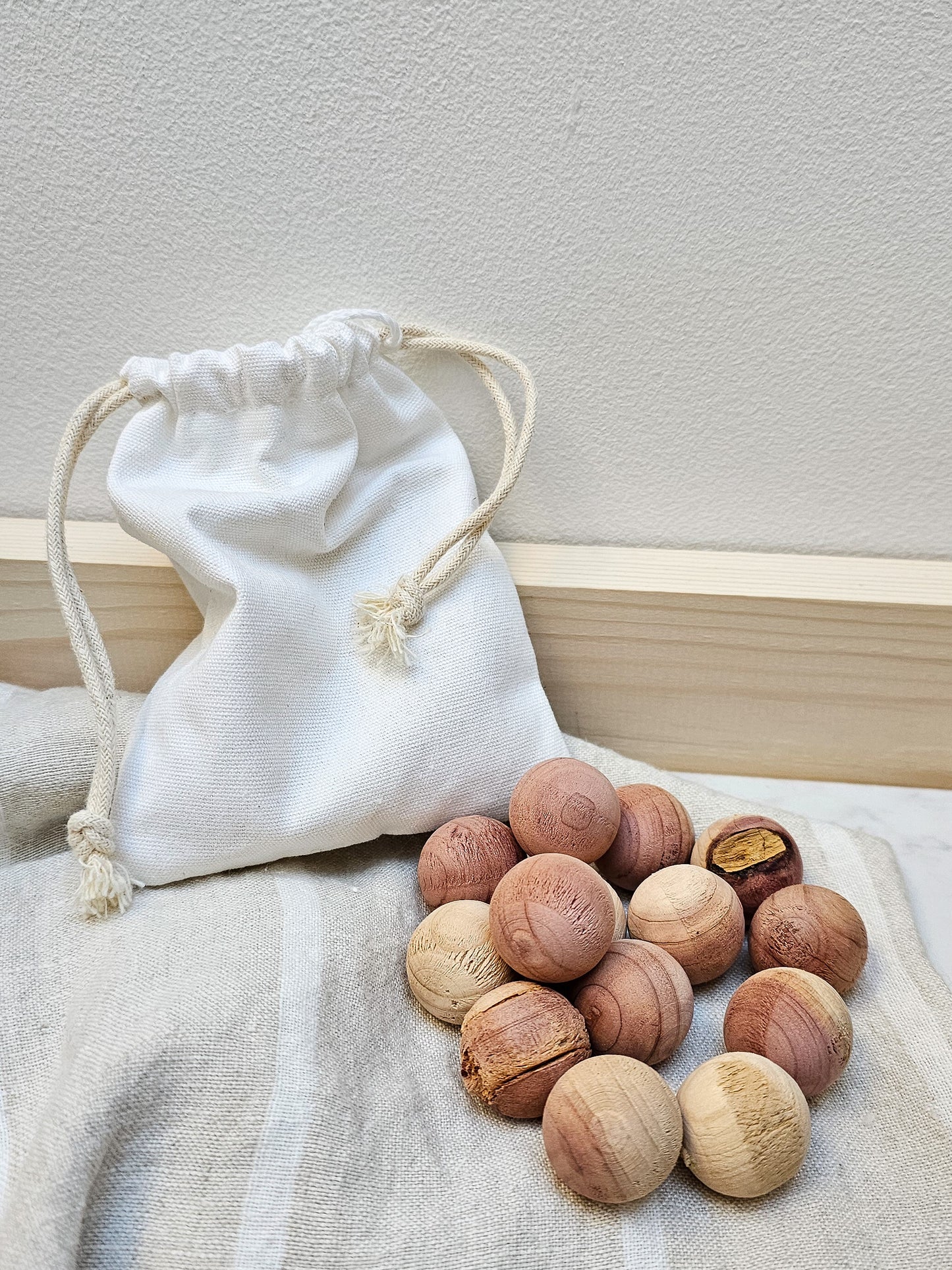 A white drawstring bag with a selection of red cedarwood moth balls spilling out onto a light surface.