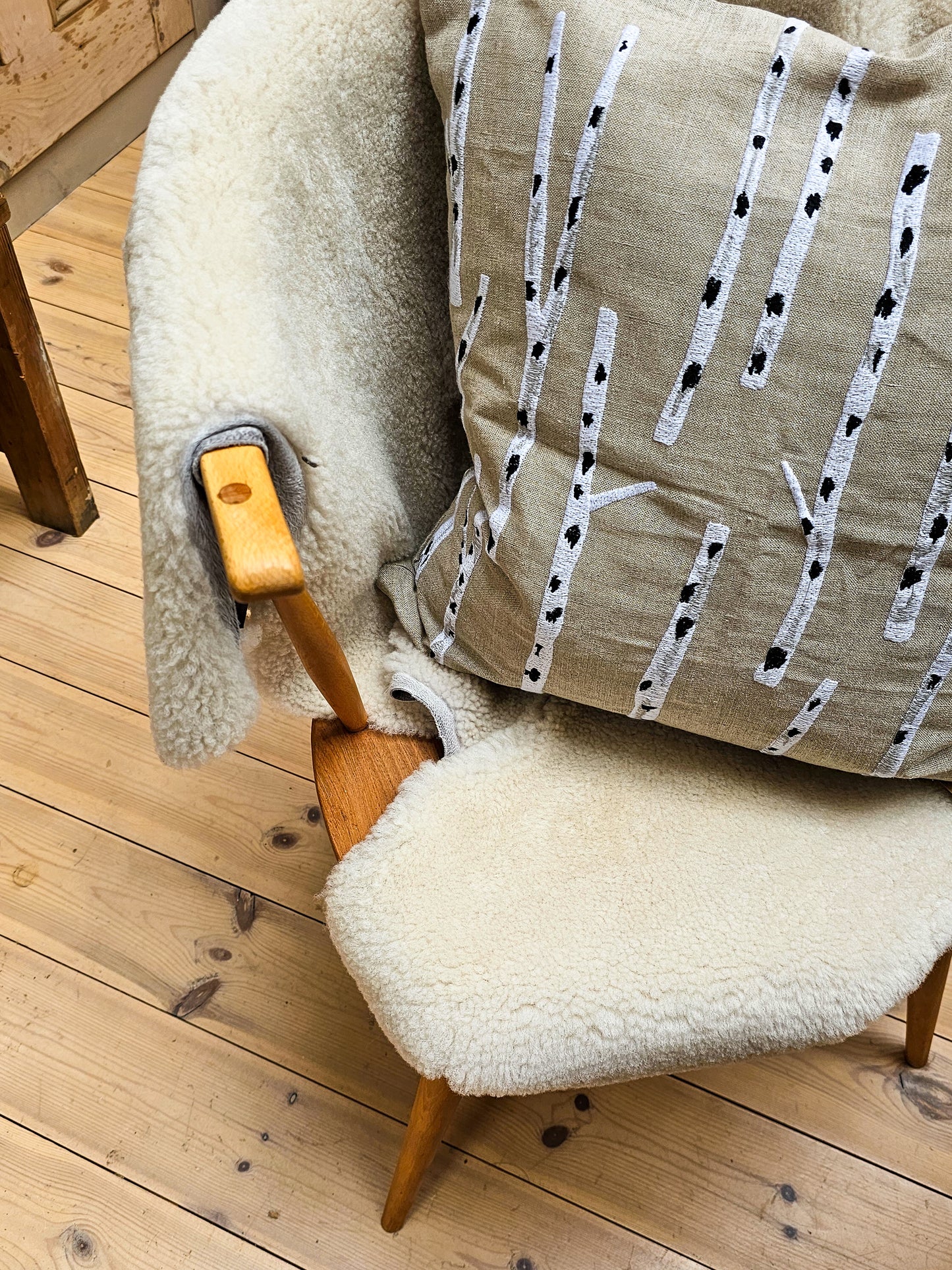 Chair with a sheepskin and cushion featuring a black and white pattern on a wooden floor.
