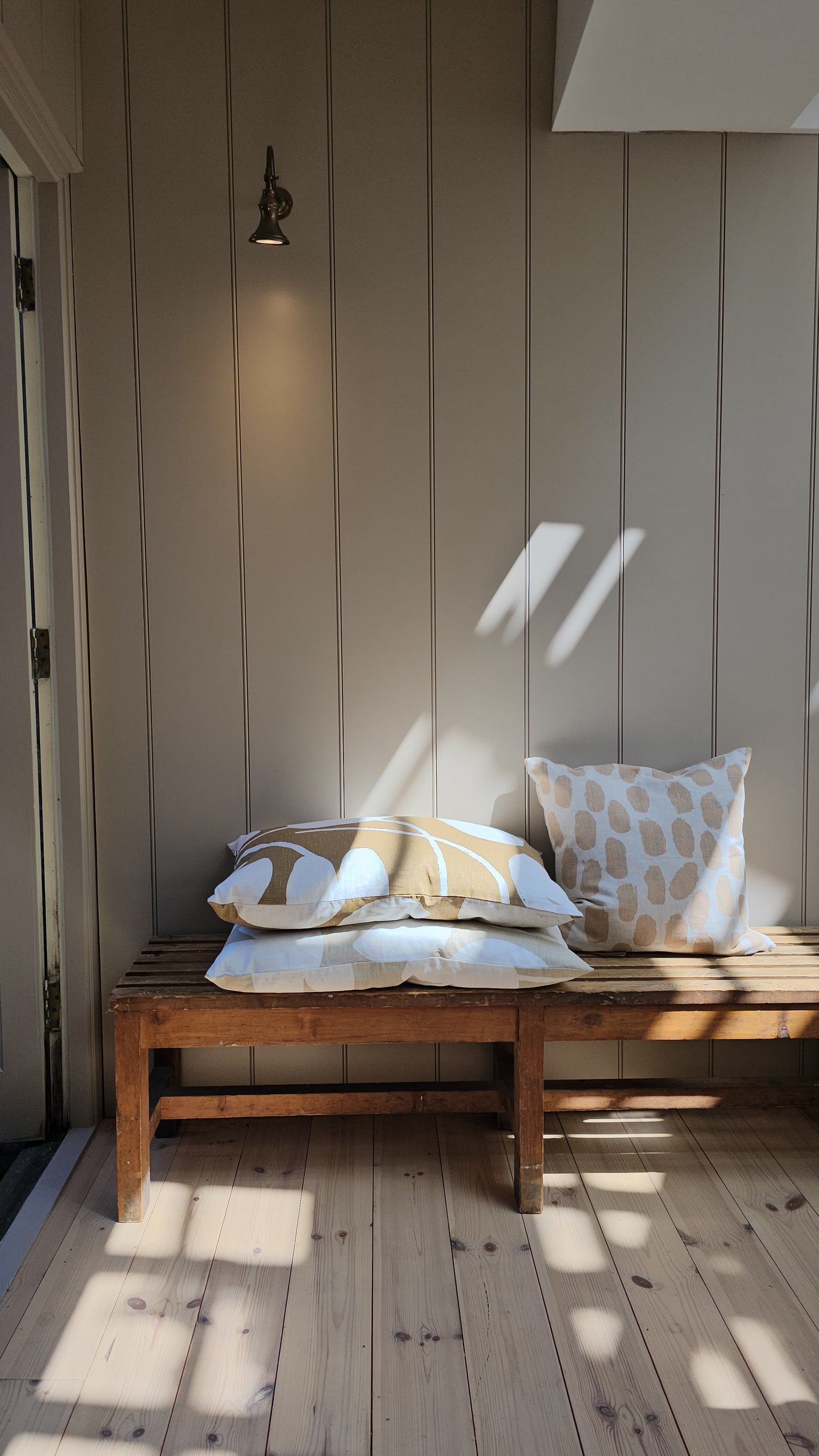 Vintage wooden bench with cushions against a paneled wall on a wooden floor