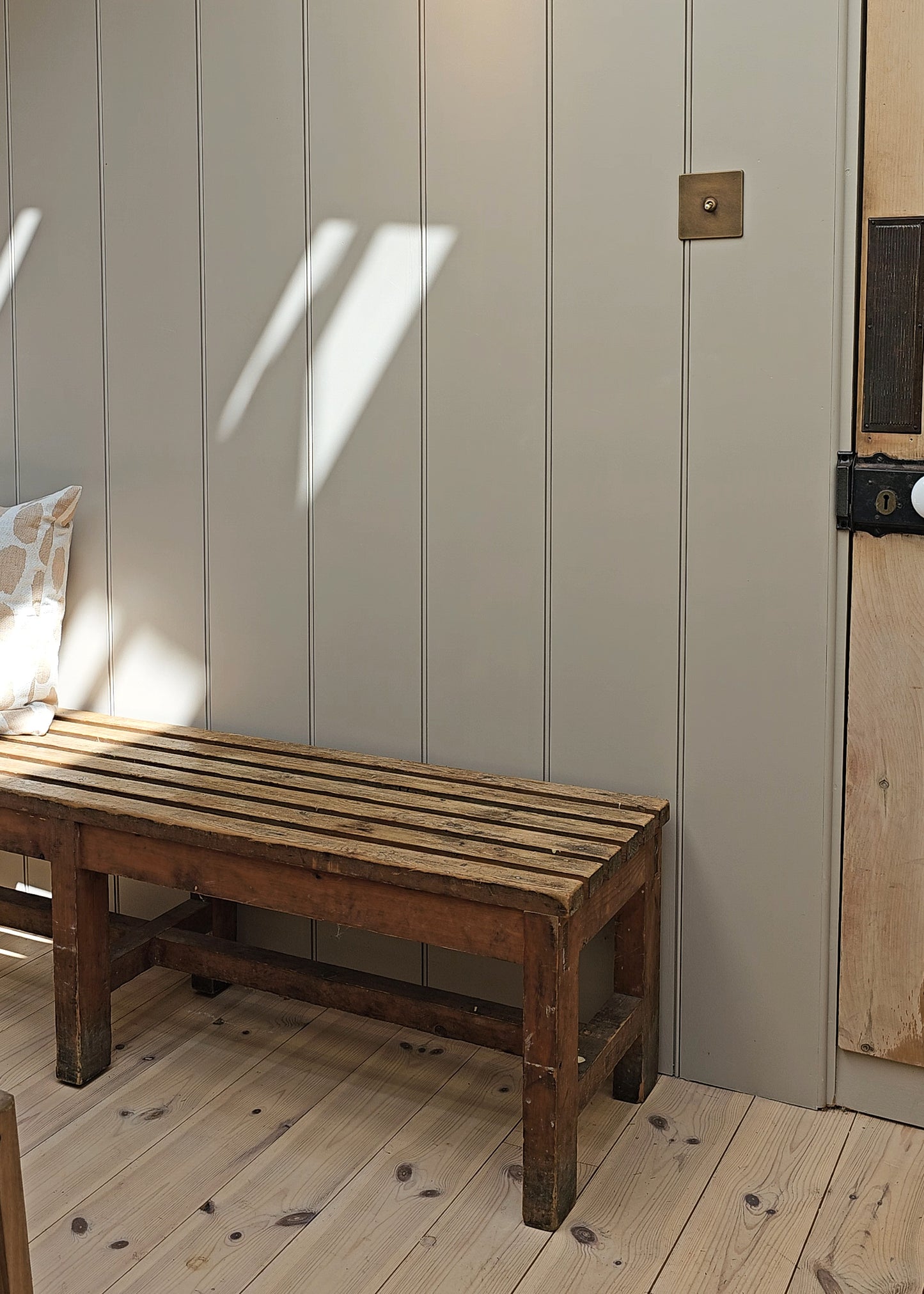 Wooden bench against a paneled wall with natural light casting shadows.
