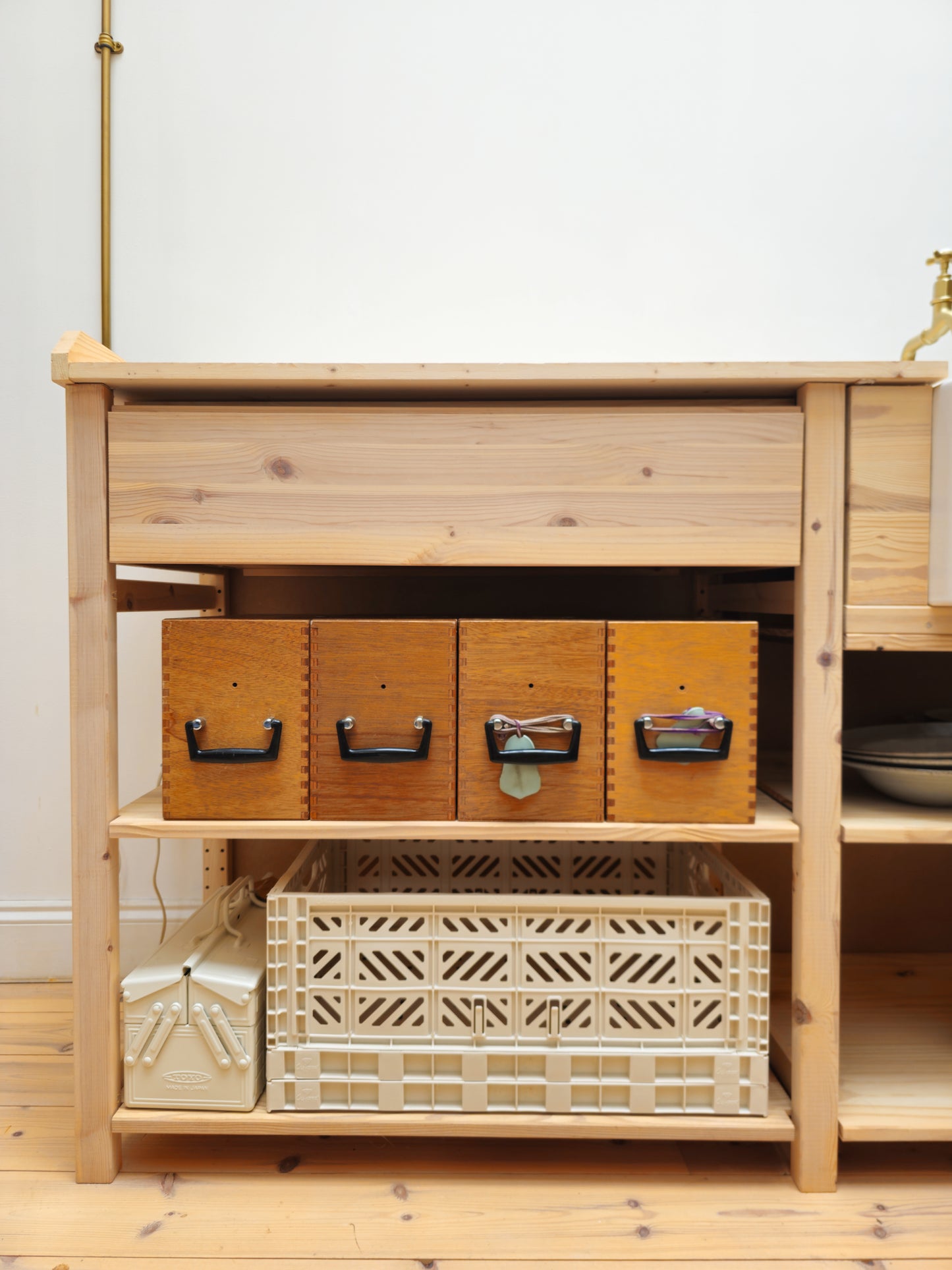 Wooden shelf with storage boxes and crates against a white wall.