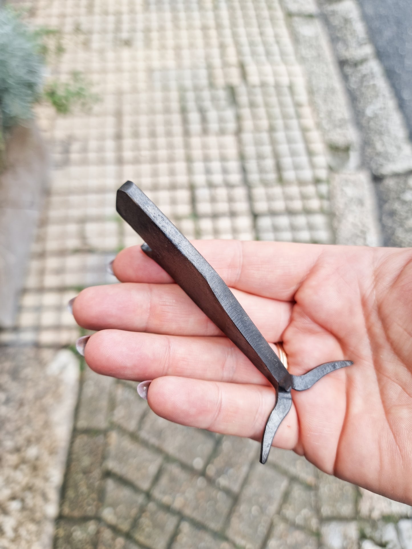 The top of a hand forged iron bottle opener shaped like a whale, held in an open palm.