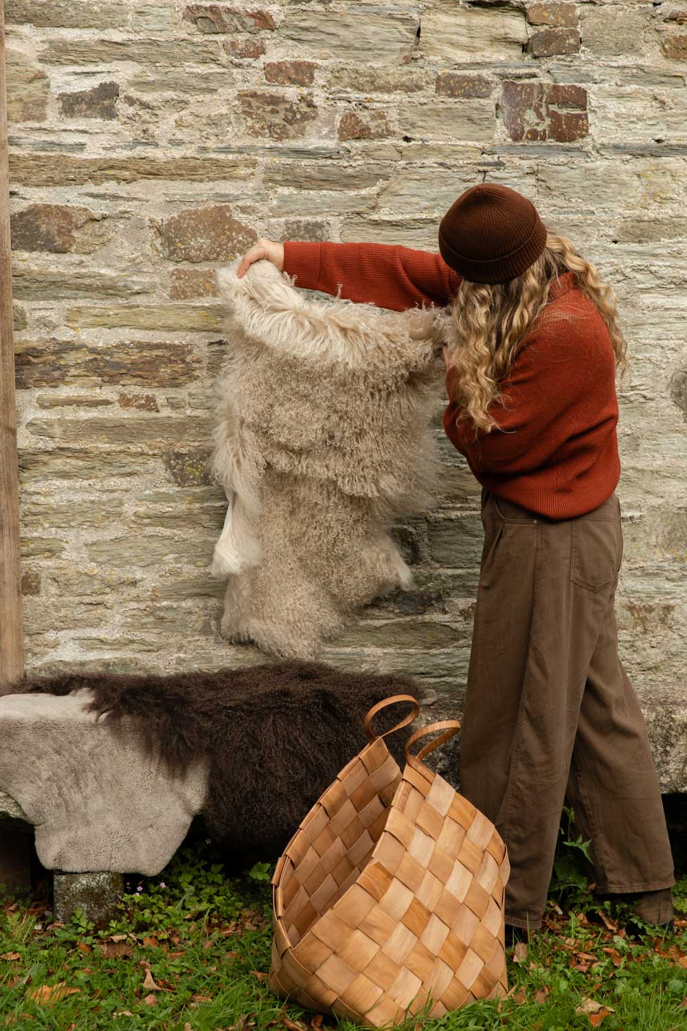 Cream Tibetan sheepskin rug held up against a stone wall, with a brown sheepskin on a granite bench and a woven basket